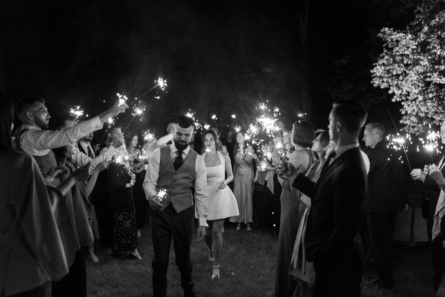 Wedding couple dances surrounded by guests holding sparklers during a magical nighttime celebration.