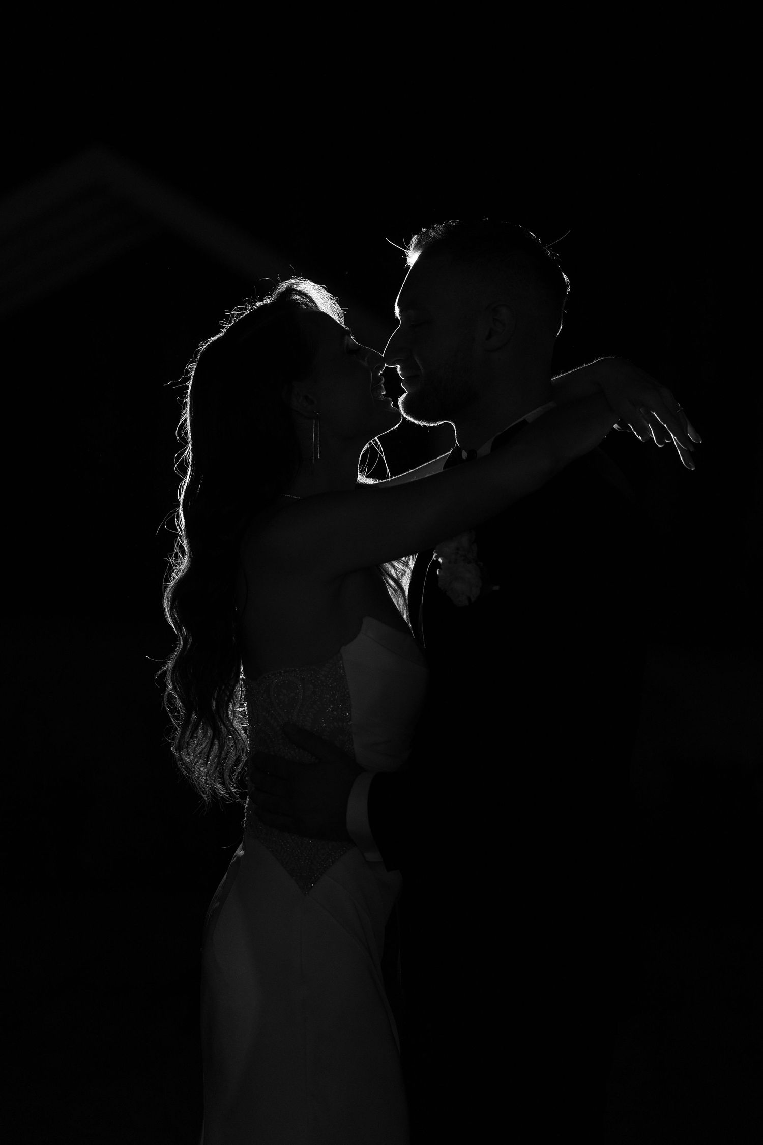 Black and white silhouette of a romantic couple embracing and about to kiss against a dark background.