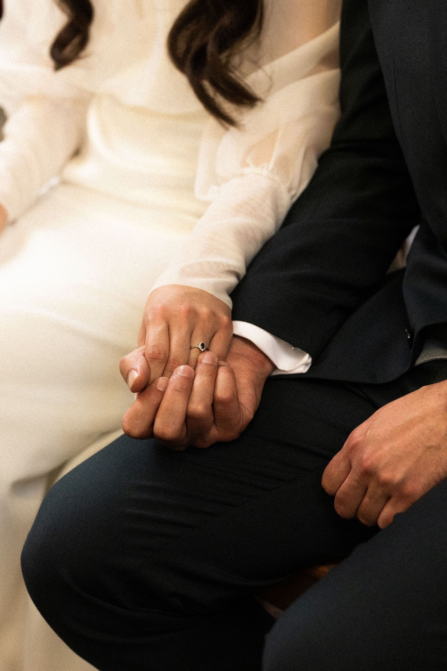A close-up shot of a couple holding hands, showing their wedding attire and an engagement ring.