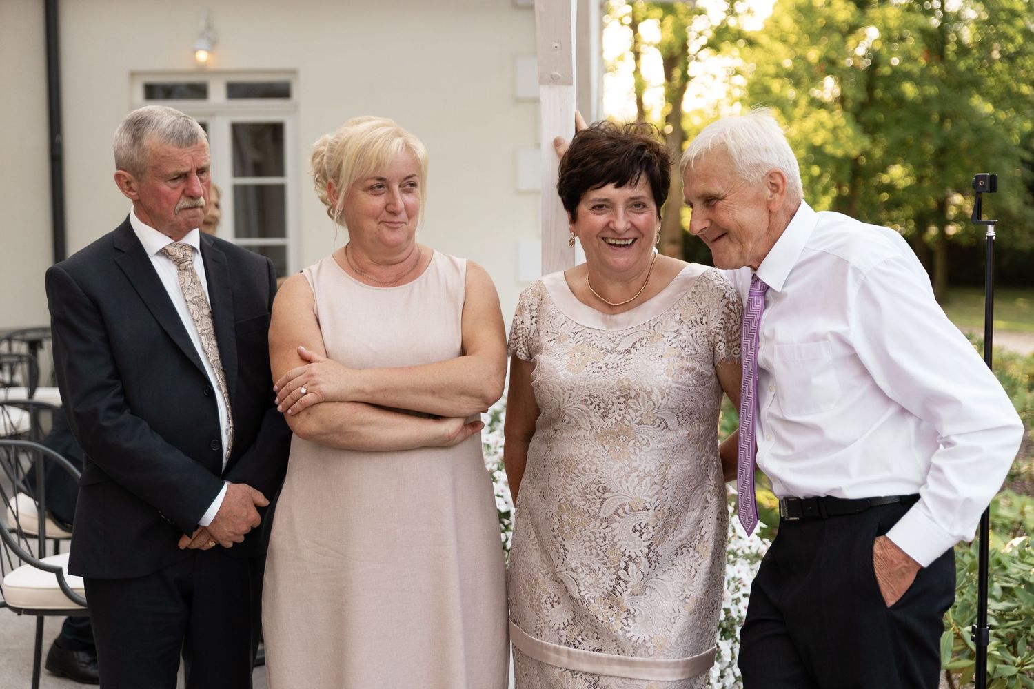 Four people dressed in formal attire stand together outdoors at a social gathering during golden hour.