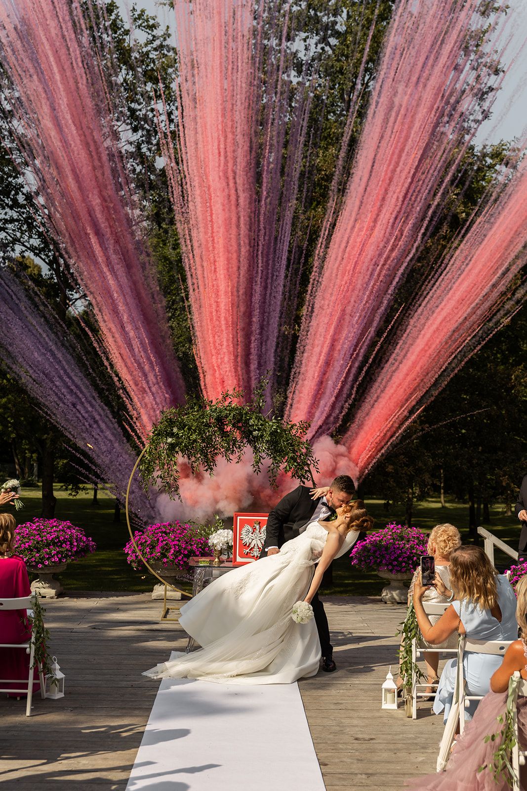 Dramatic pink and purple draped fabric creates an ethereal backdrop for an outdoor wedding ceremony.