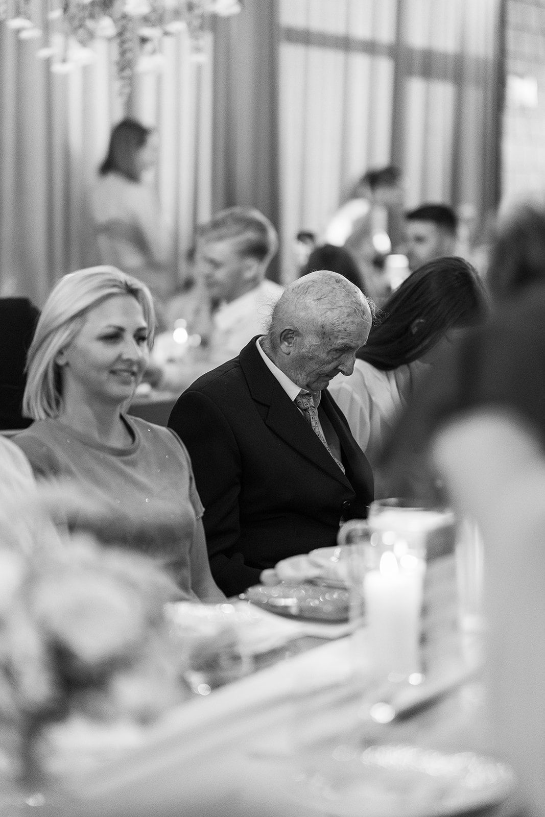 Black and white photo showing guests seated at elegant tables during a wedding reception celebration.