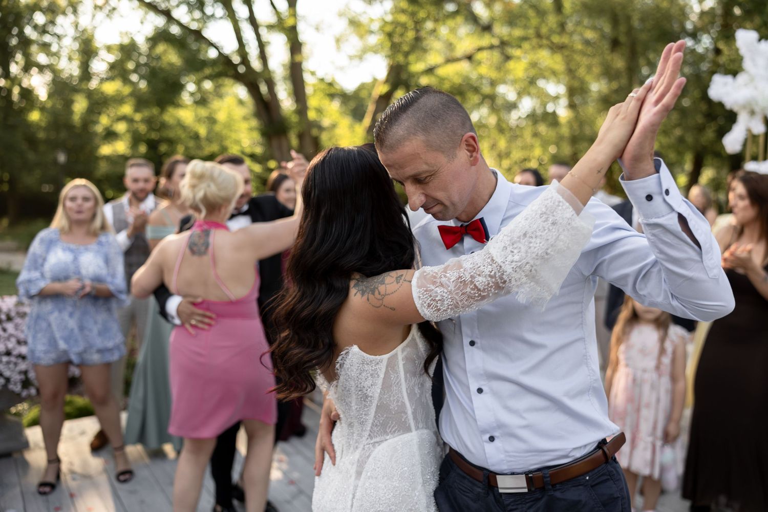 Bride and groom share first dance outdoors at wedding reception surrounded by guests in summer setting.