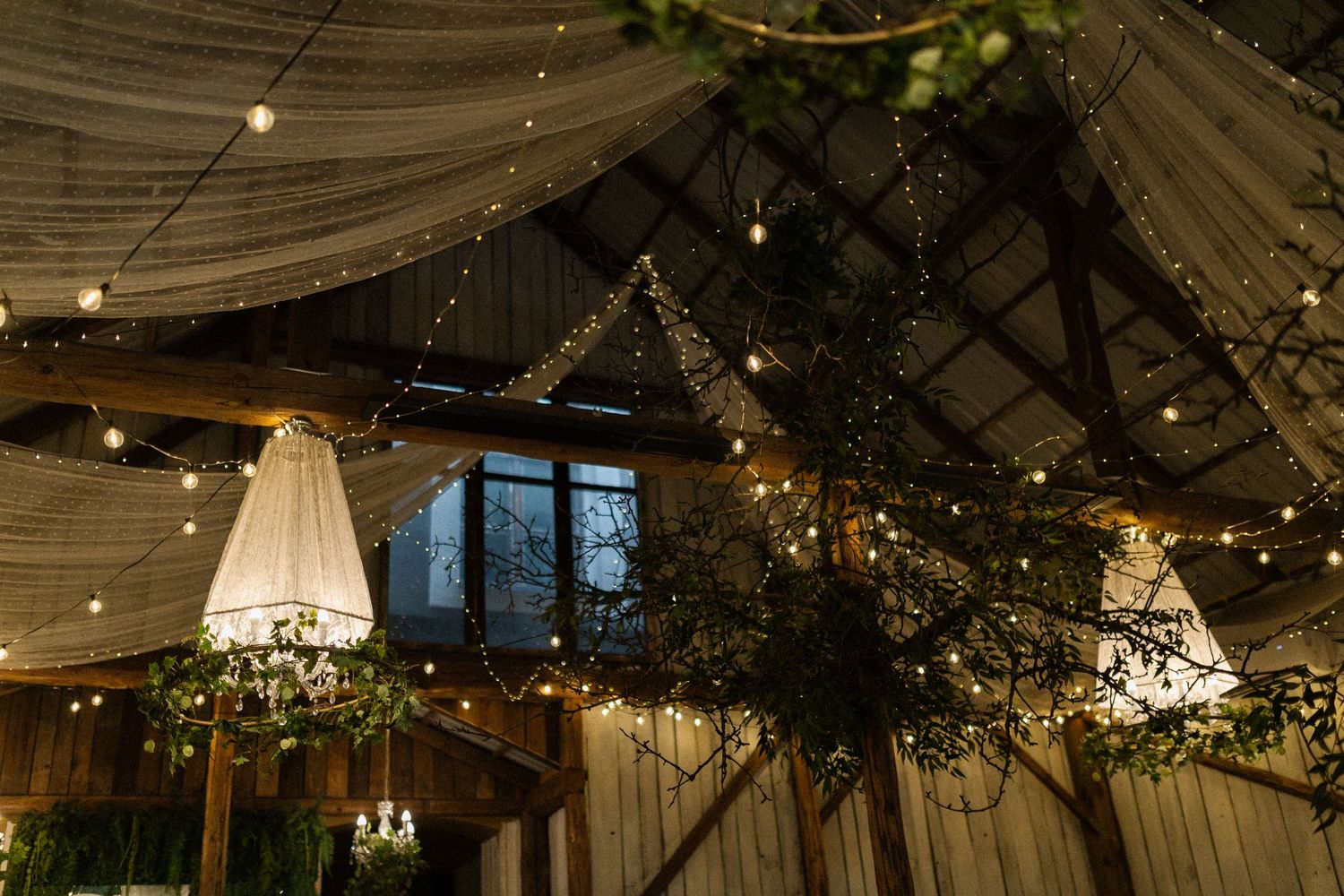 Indoor wedding venue with draped fabric ceiling, hanging white lanterns and string lights creating a romantic atmosphere.