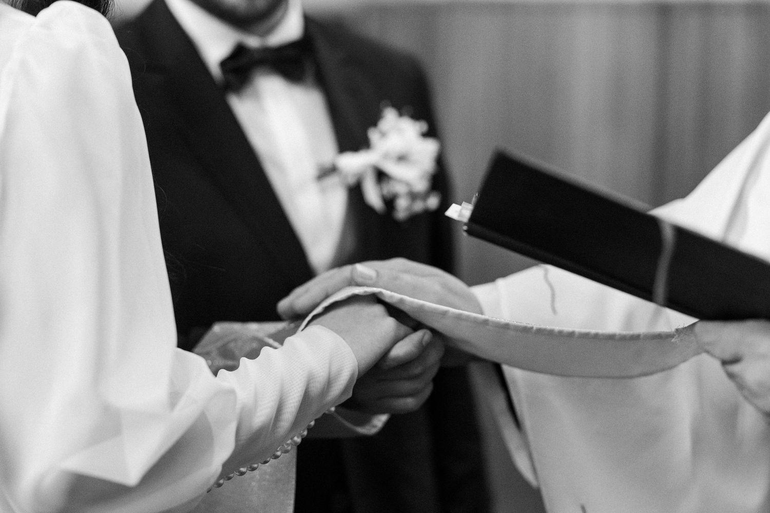 Black and white wedding ceremony photo showing hands exchanging rings with gentle focus on the jewelry.