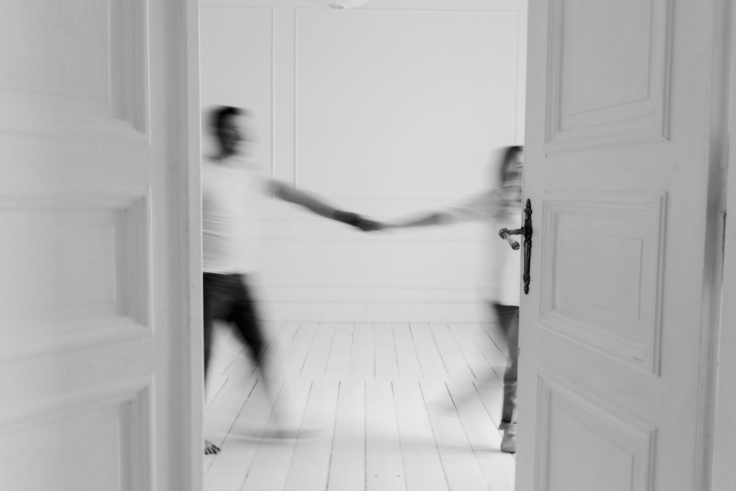 Artistic motion blur photo of two people holding hands through doorway in white room.