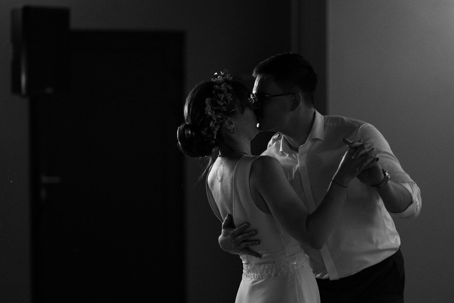 Romantic black and white photo of a couple dancing closely together in a dimly lit room with backlight silhouette.