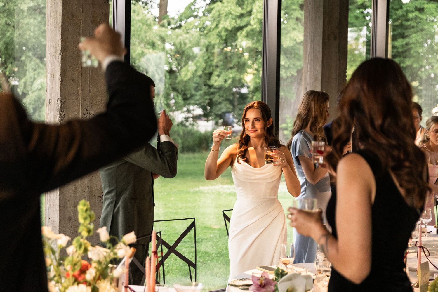 People celebrate and take photos during an outdoor reception at a rustic venue with natural greenery in the background.