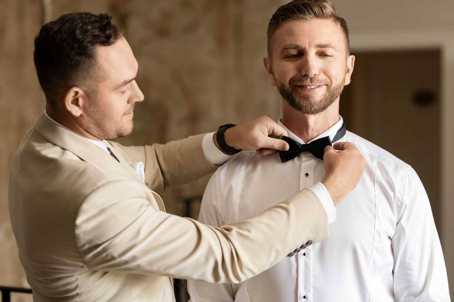 Someone helps adjust a bowtie on a person wearing a white dress shirt during formal preparation.