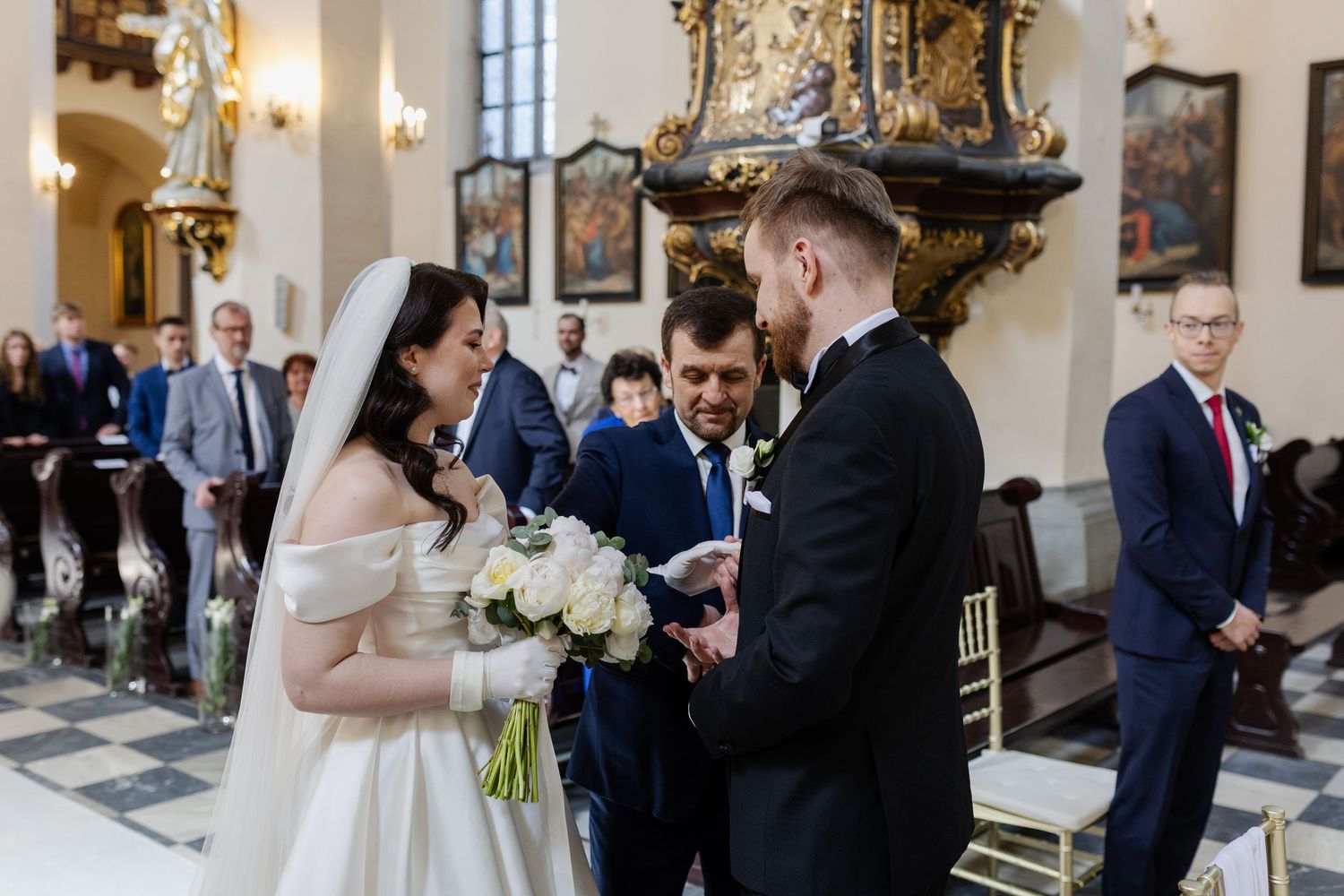 A couple exchanges vows during their wedding ceremony inside an ornate church with golden decorative elements.