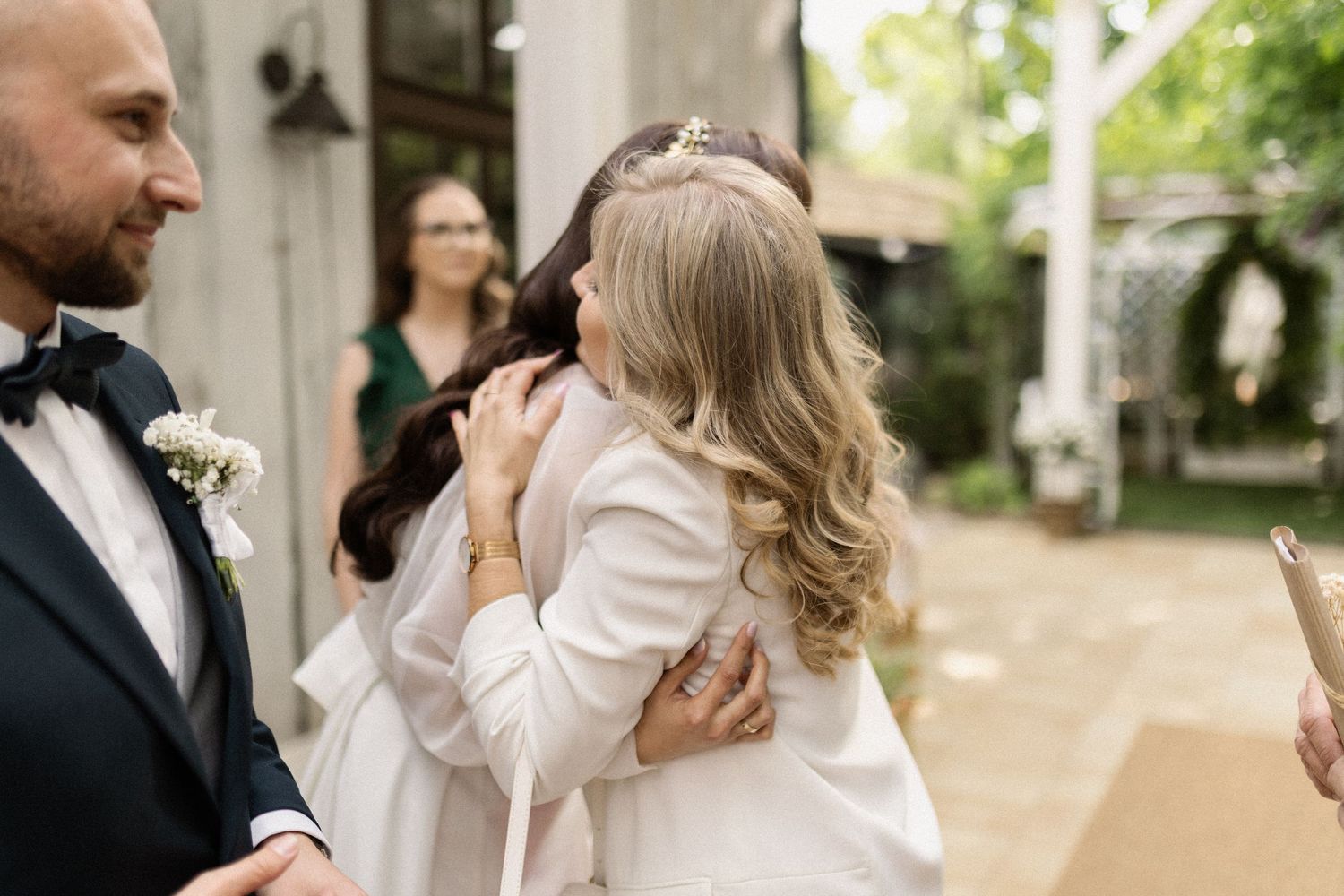 A woman in a white jacket wipes her tears during an emotional outdoor wedding ceremony.