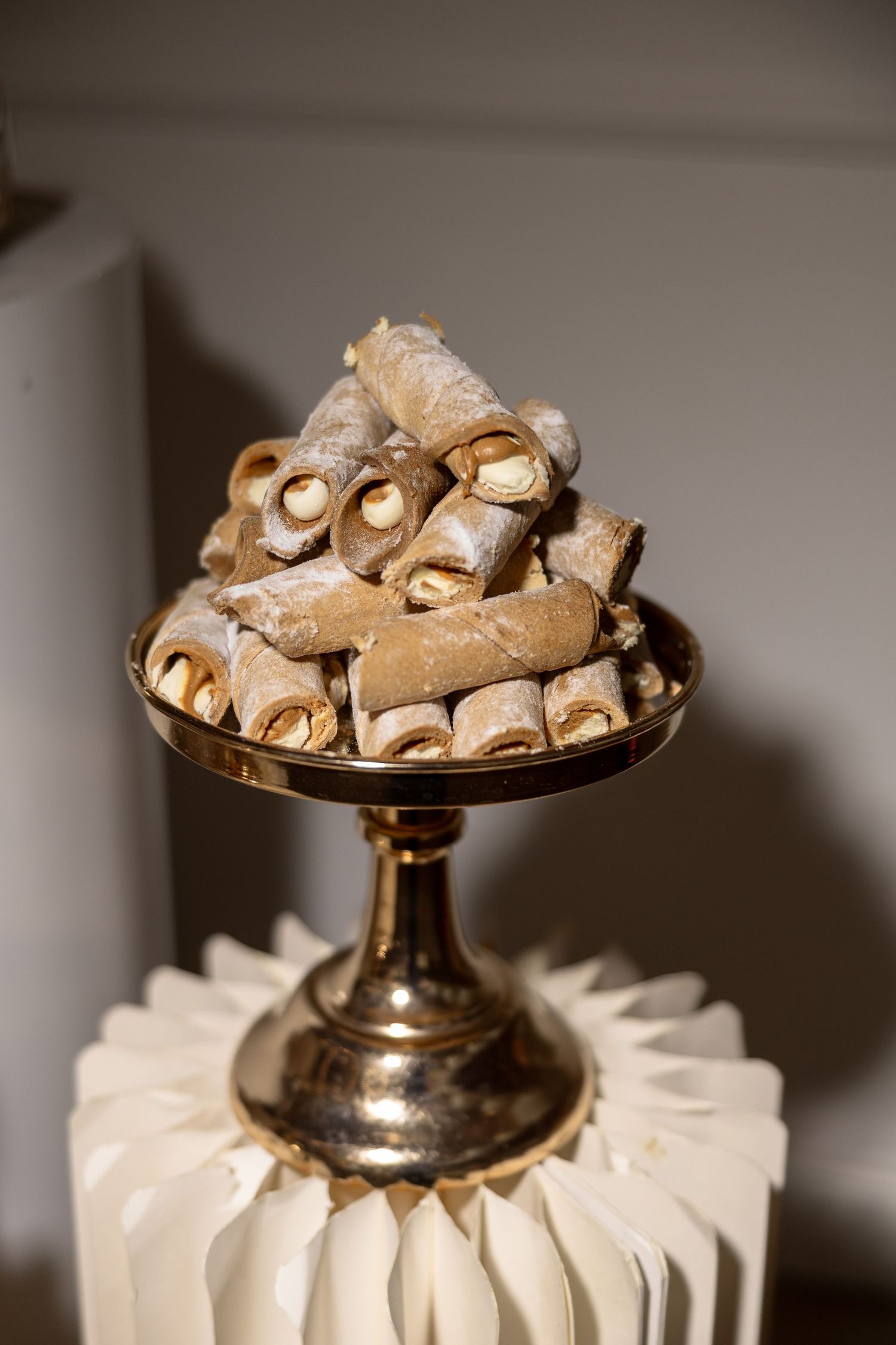Golden pedestal stand displaying a pile of rolled wafer cookies dusted with powdered sugar at an elegant event.
