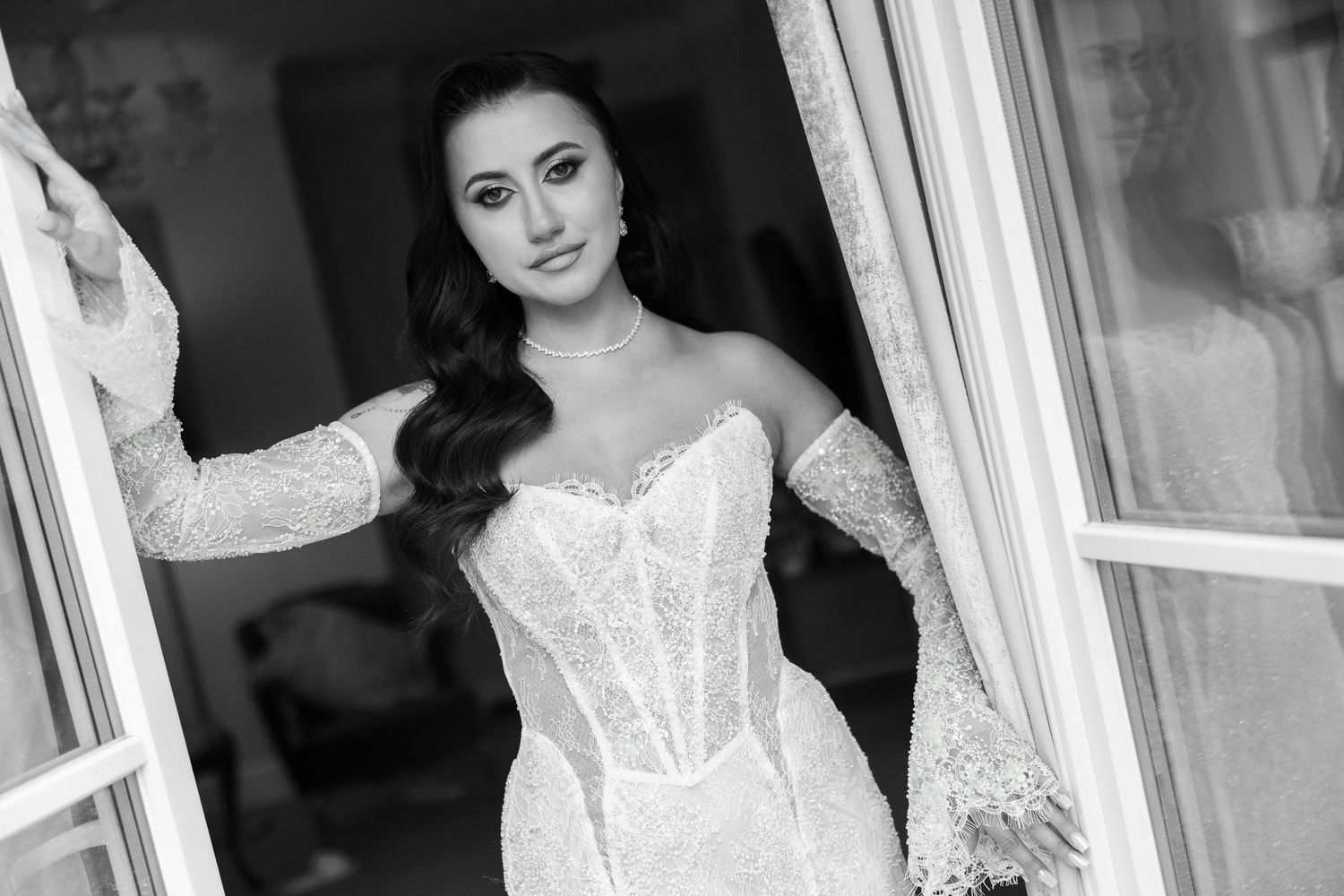 Elegant bride in lace corset wedding gown posing in doorway, black and white bridal portrait photography.