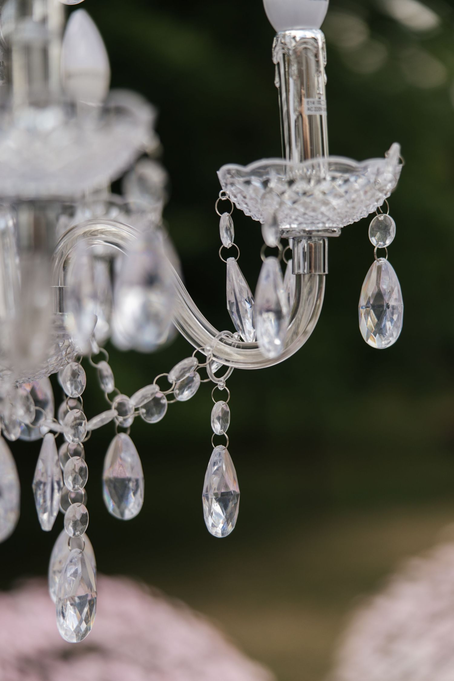 Close-up of elegant crystal chandelier with teardrop pendants and curved glass arms, sparkling against a soft bokeh background.