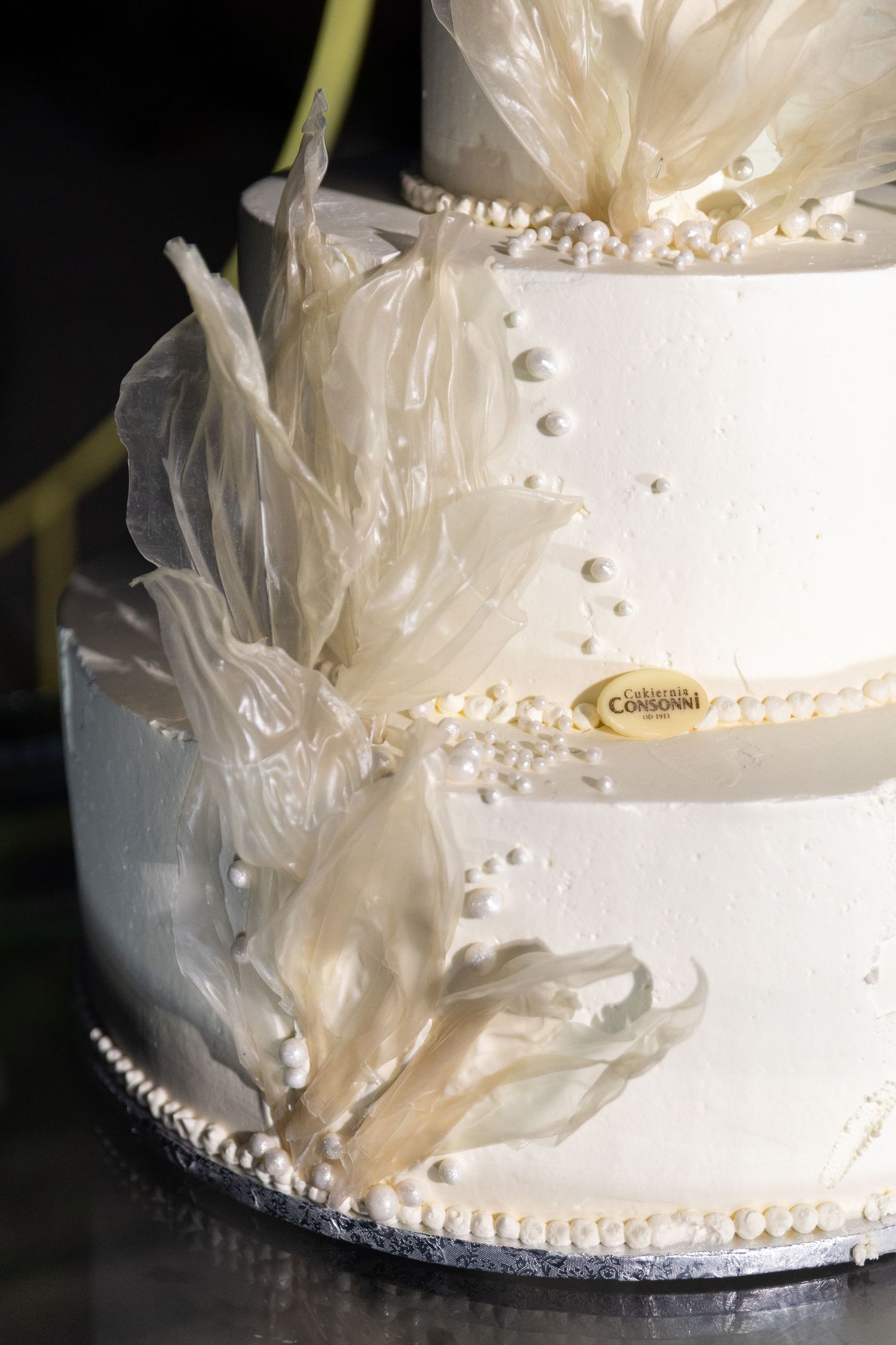 Close-up details of a white wedding cake decorated with delicate tulle fabric and pearl accents along the tiers.