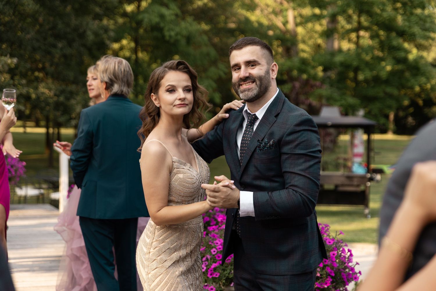Wedding guests enjoy cocktail hour outdoors with pink floral arrangements and formal attire.