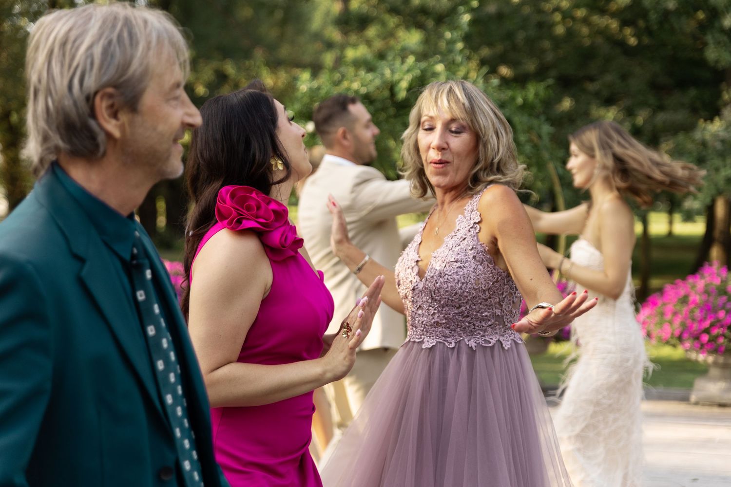 A group of wedding guests dance and celebrate together in an outdoor garden setting.