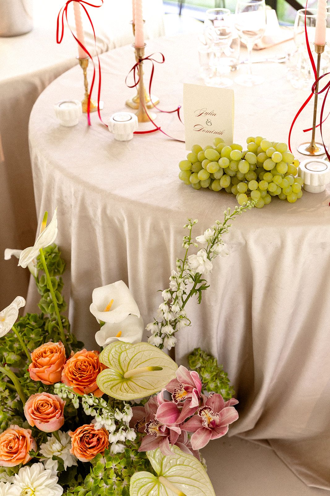 Elegant wedding reception table with white linens, peach roses, green grapes, and delicate white floral arrangements.
