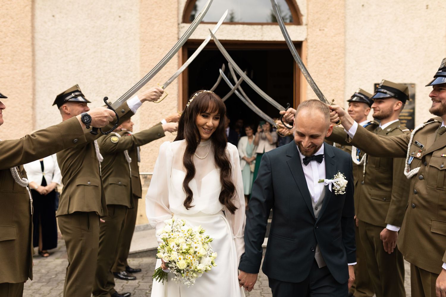 A military honor guard raises swords as a bride and groom exit their wedding ceremony under the traditional sword arch.