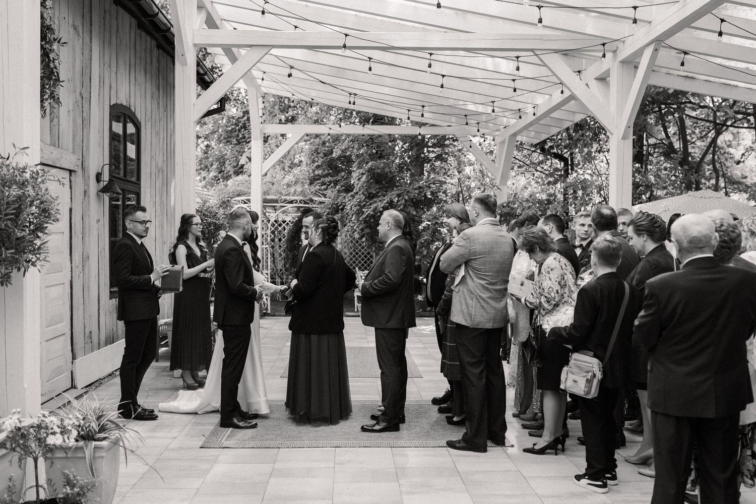 Wedding guests gather under a covered patio area during an outdoor black and white celebration reception.
