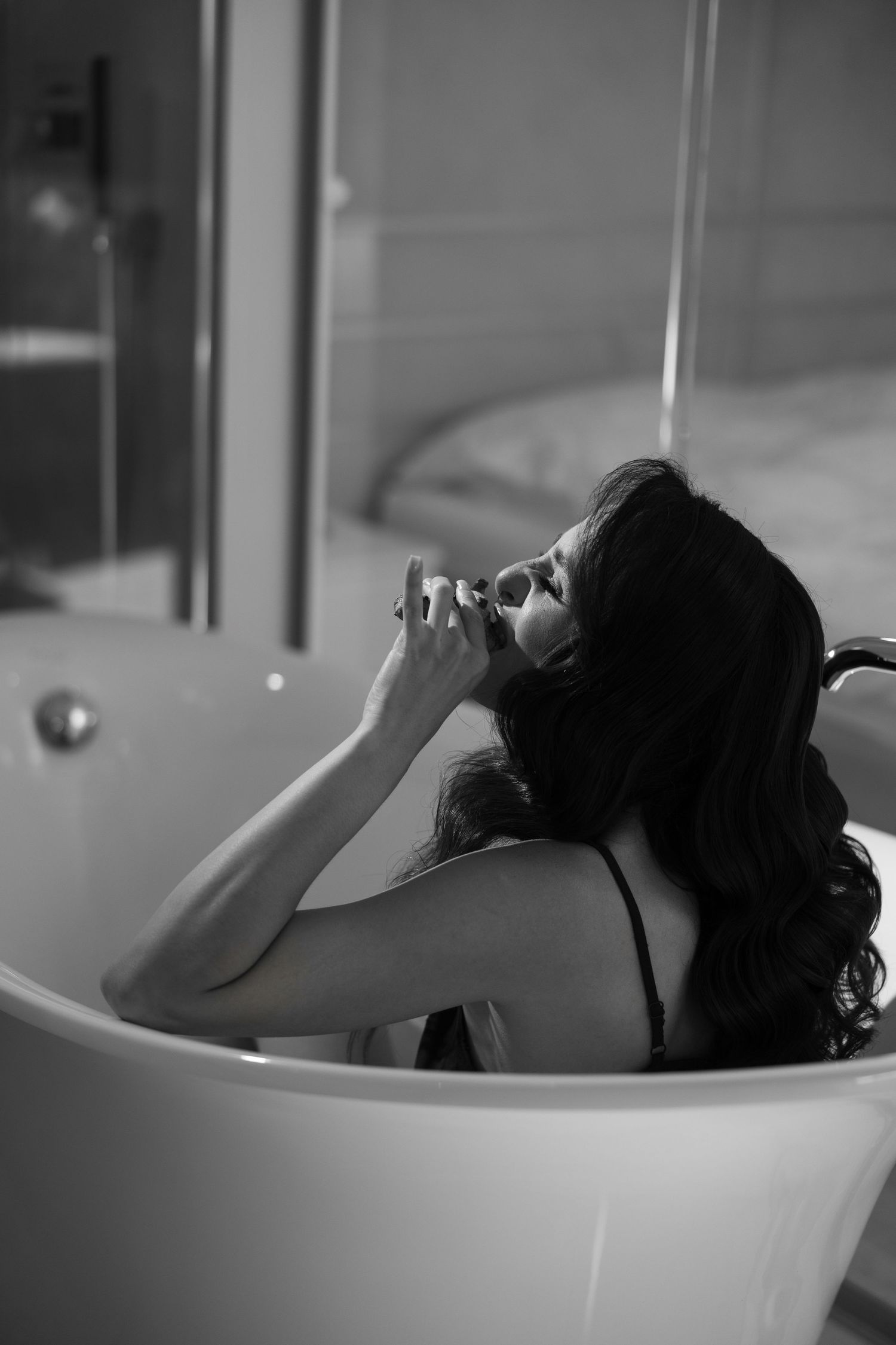 Black and white photo of woman relaxing in freestanding bathtub in luxury bathroom.