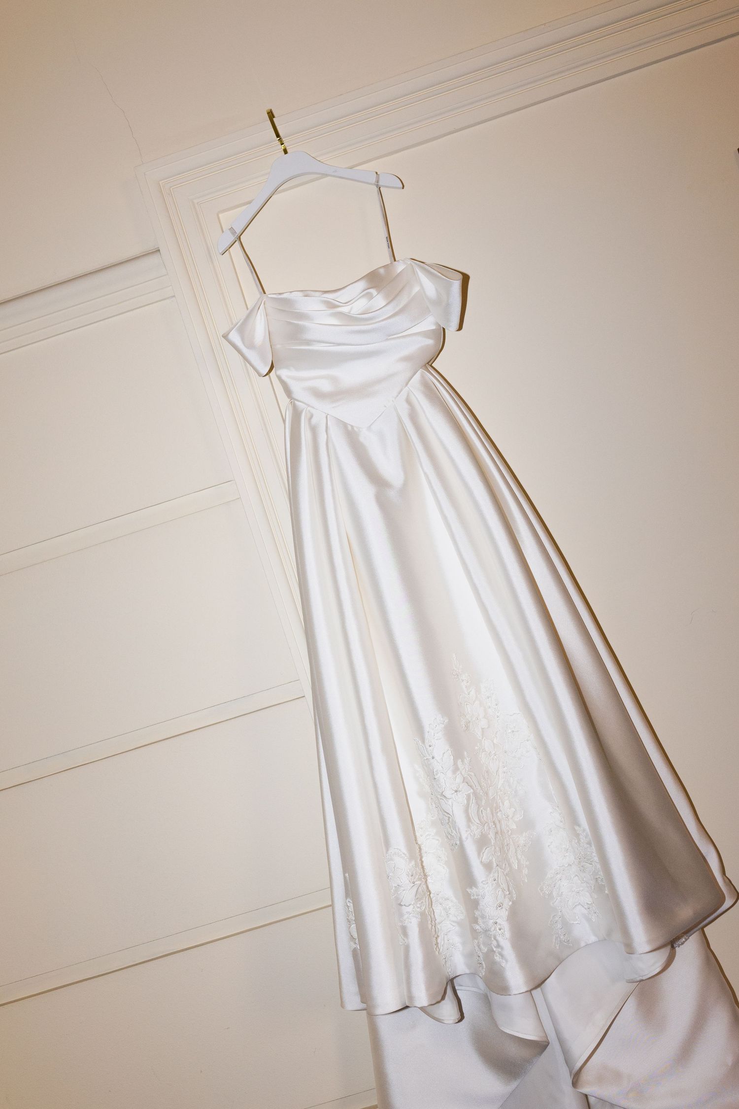 A white satin wedding dress with a strapless silhouette and delicate embroidered details hangs elegantly on display.