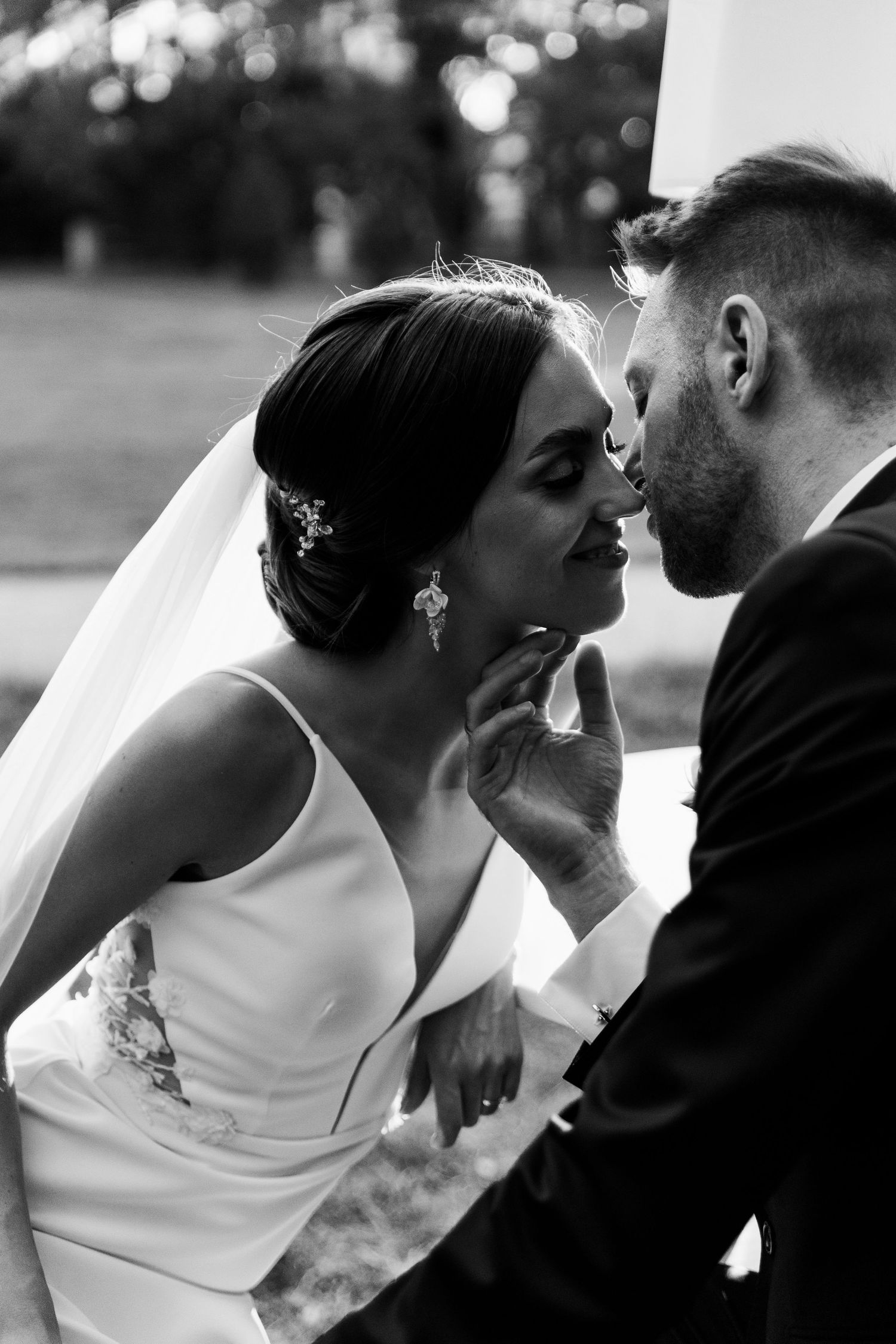 Black and white romantic wedding portrait showing a tender moment between newlyweds in an outdoor setting.