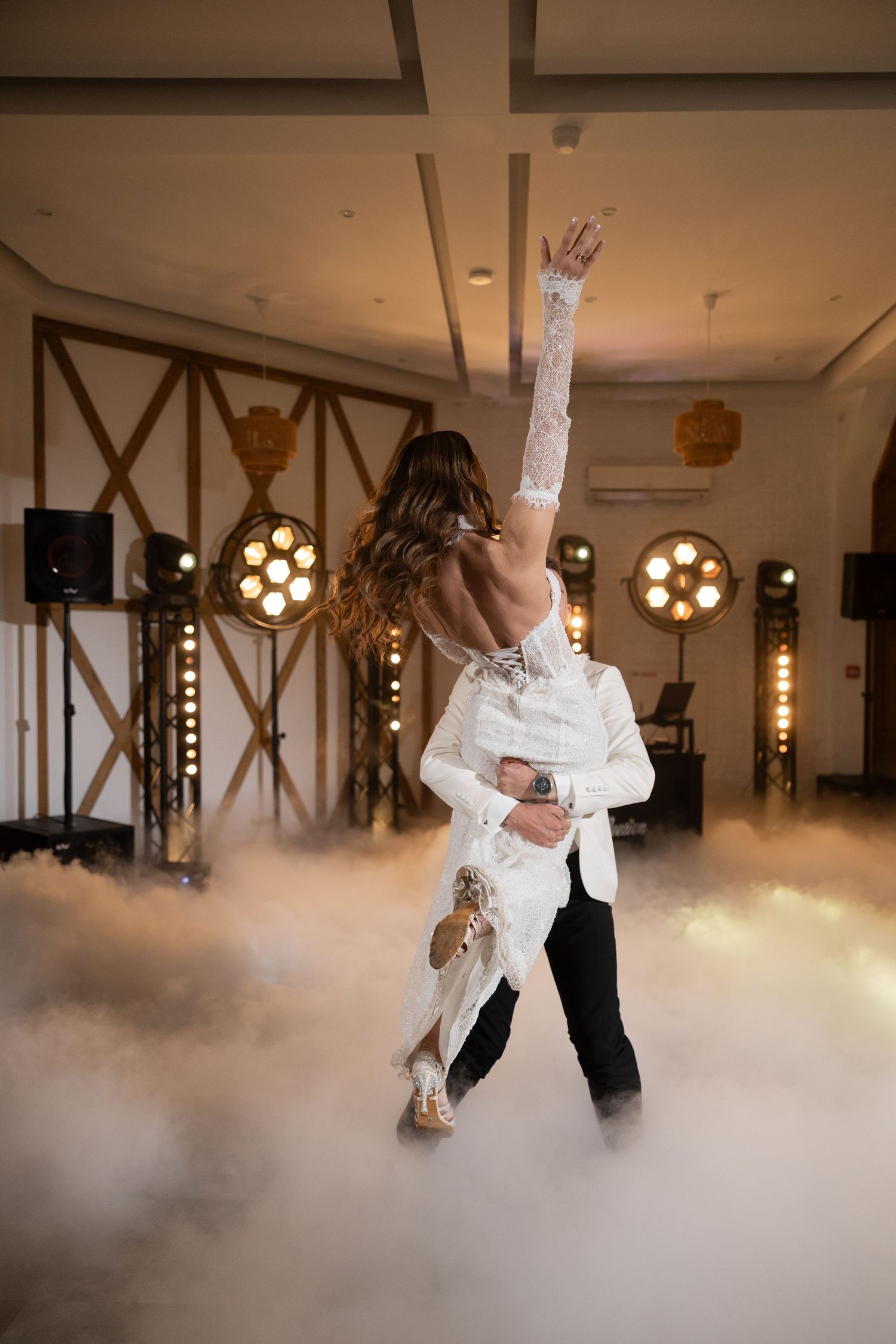 Bride and groom share first dance surrounded by dramatic fog and stage lights at elegant wedding reception.