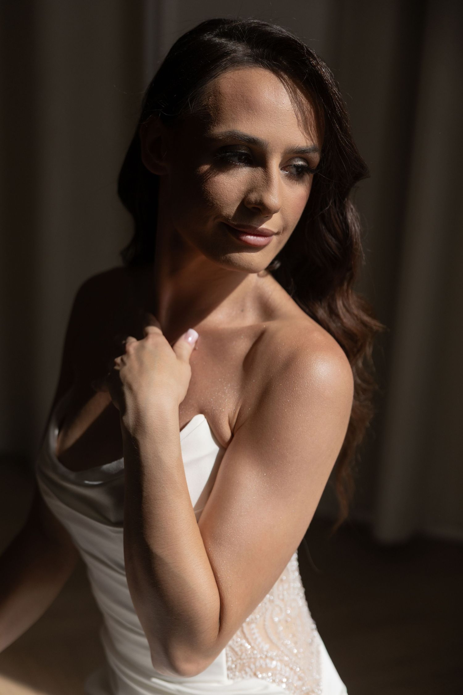 Elegant bride in a white strapless gown posing in soft natural light with glamorous hair and makeup.