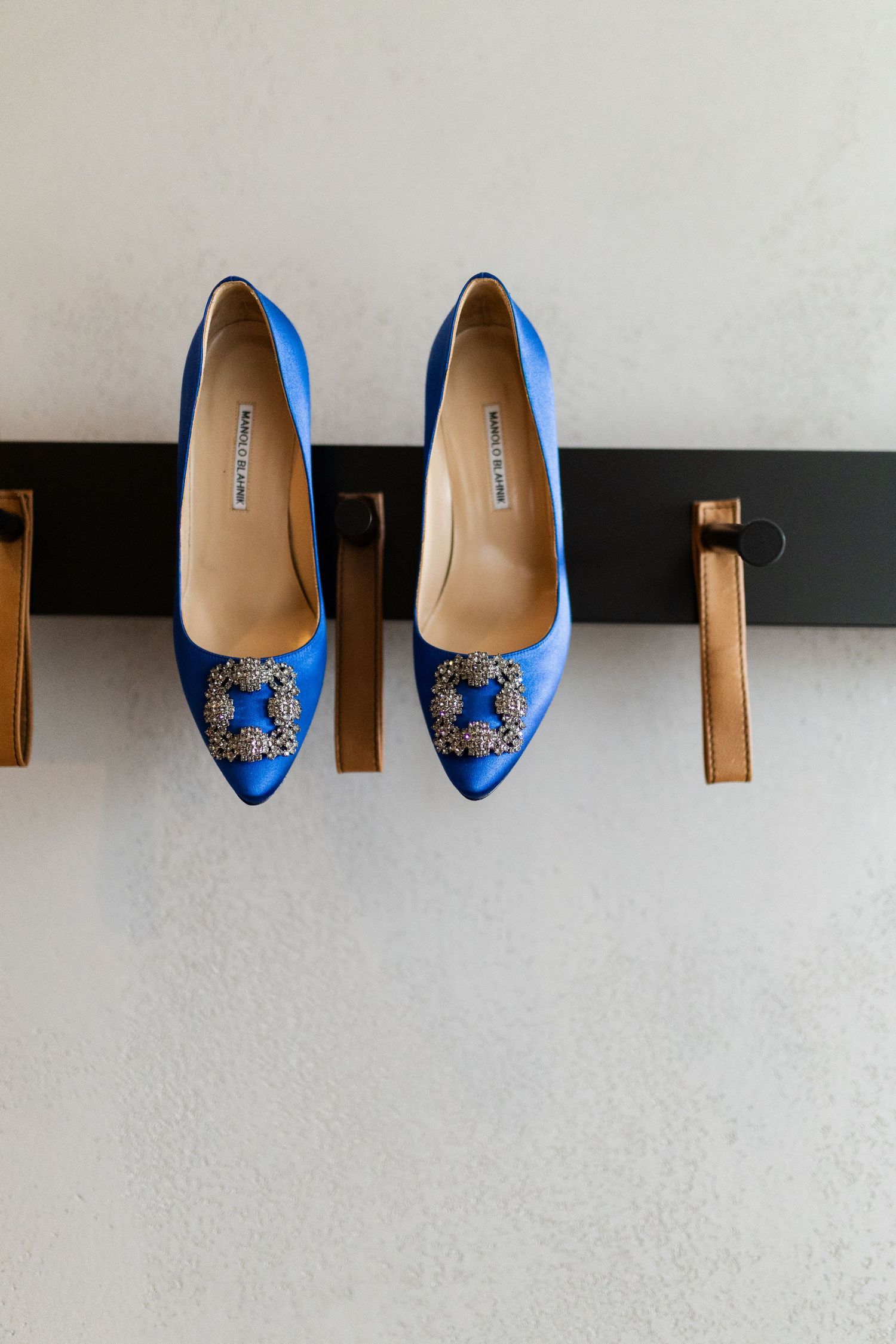 Elegant royal blue satin wedding shoes with ornate crystal brooch detail displayed on a wooden wall mount.