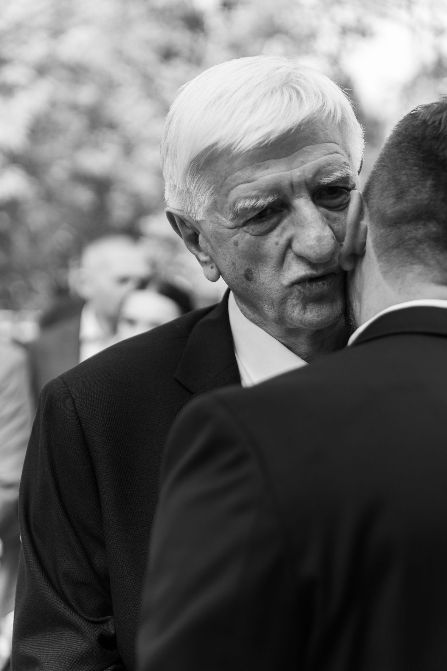 A series of black and white photographs showing two men in suits embracing or whispering to each other.