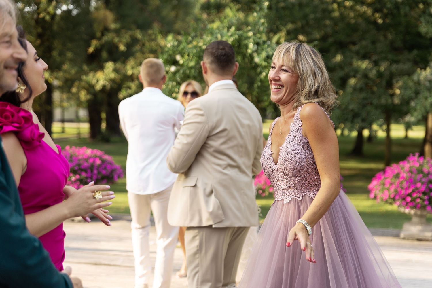 A group of people dancing and celebrating outdoors in formal attire with pink floral decorations in the background.