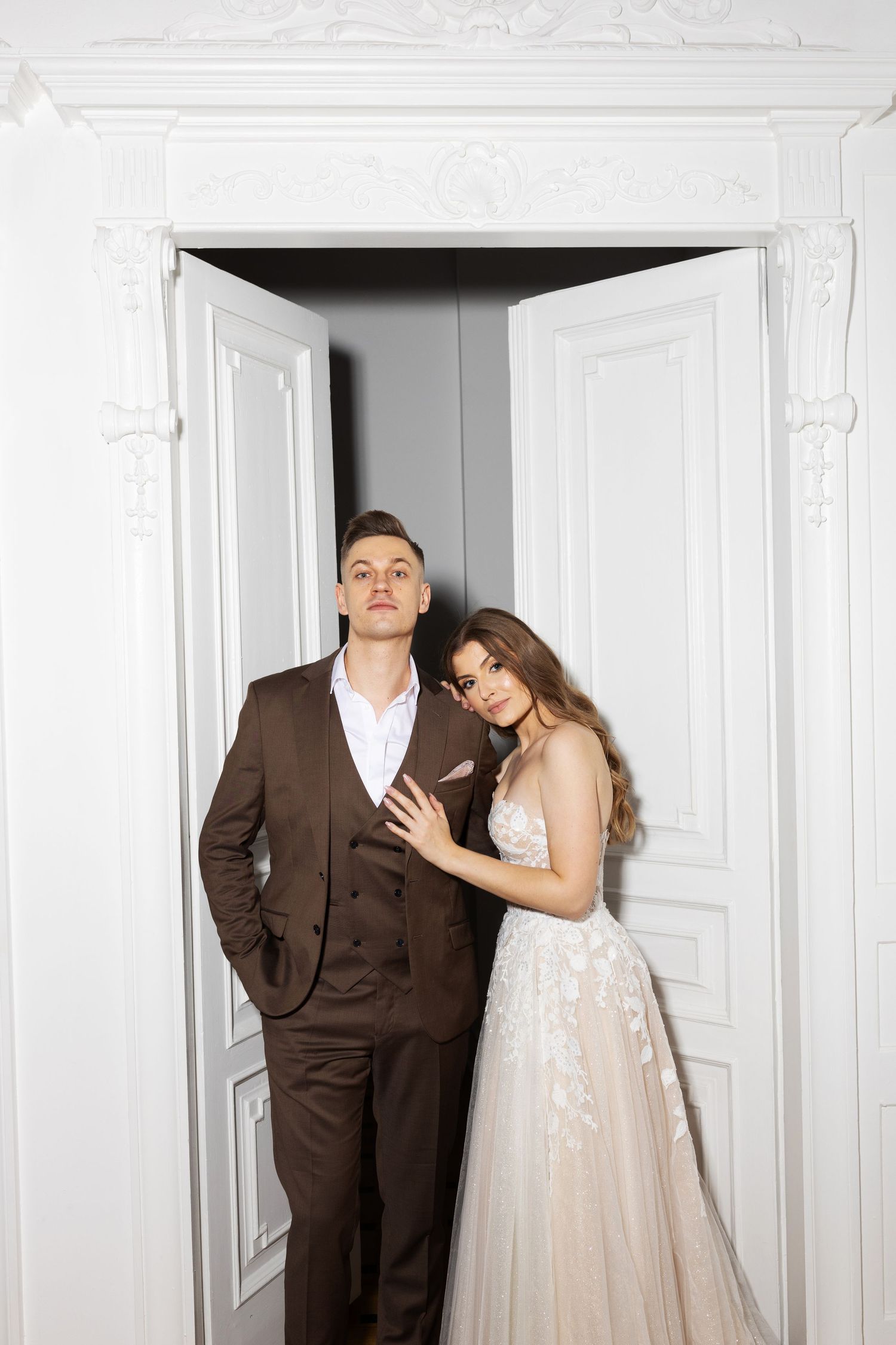 Romantic wedding portrait of couple posing in doorway with white ornate architectural details.