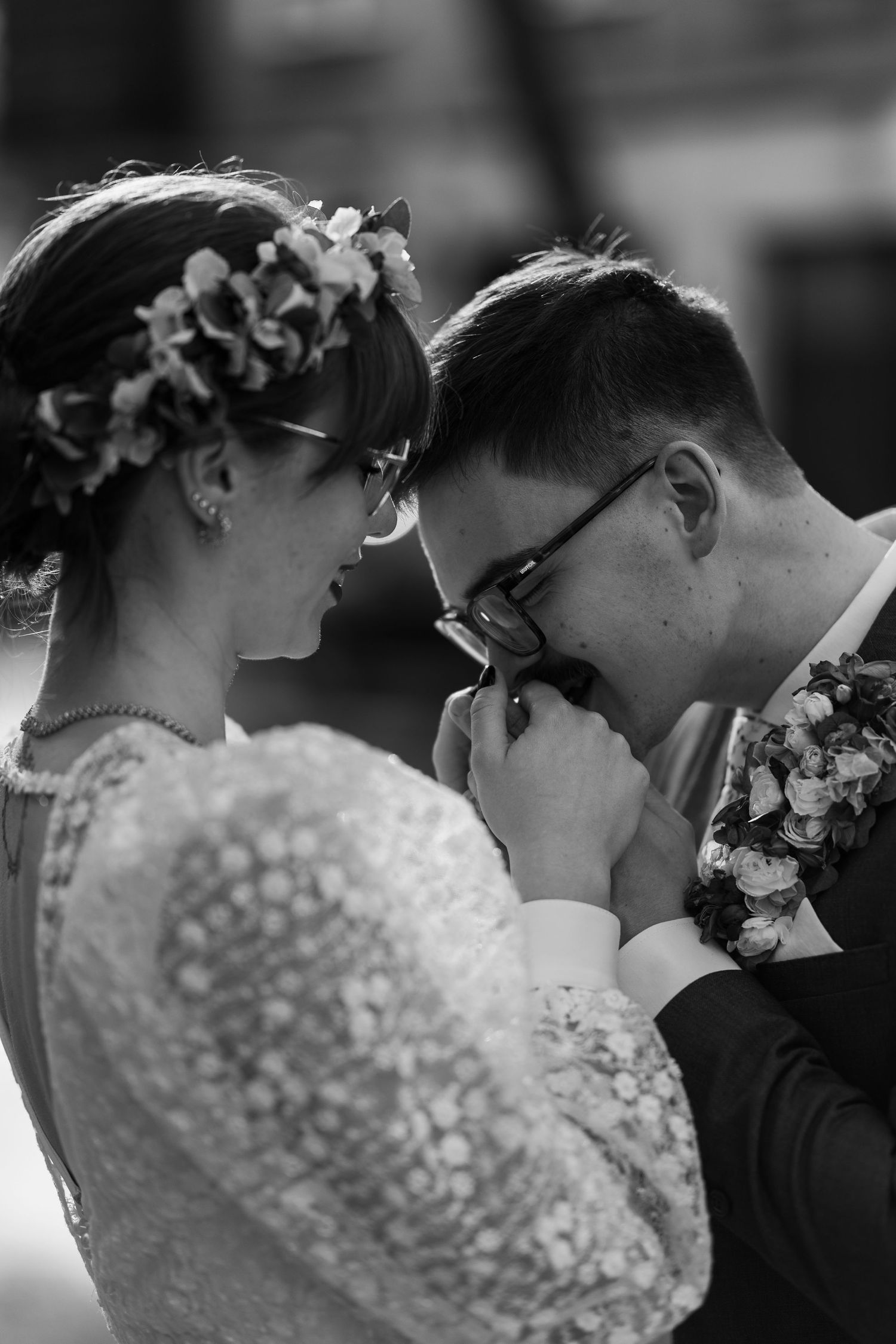 Intimate black and white wedding moment showing couple in lace dress and suit sharing emotional gesture with floral crown.