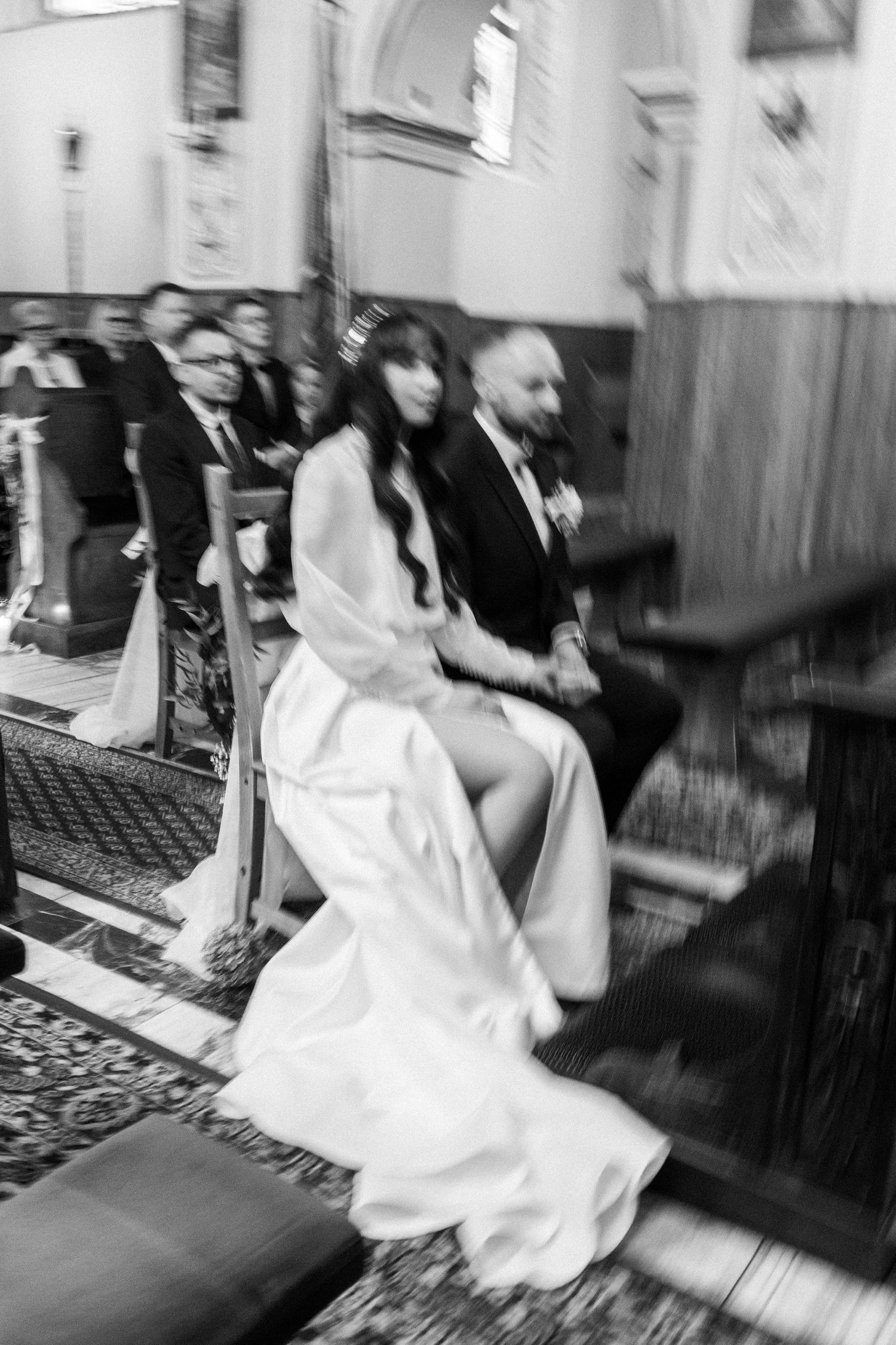 A black and white photograph shows a bride and groom seated during their wedding ceremony at a church.