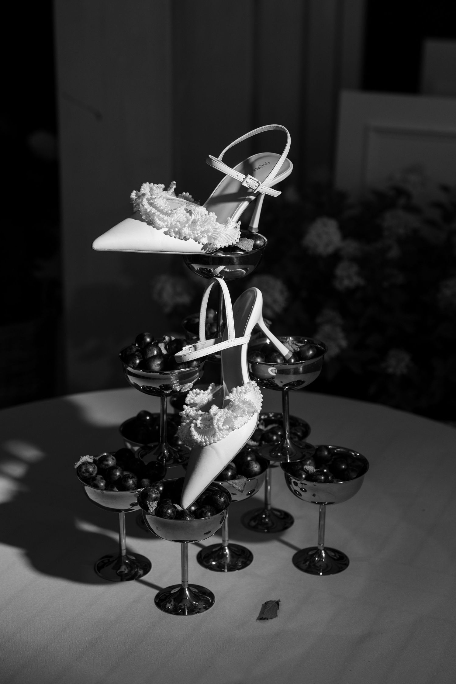 Black and white photo of bridal heels displayed on a champagne tower with decorative floral accents at a wedding reception.