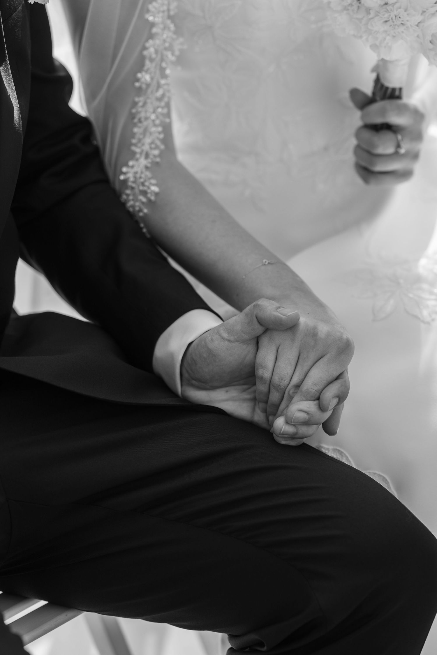 Black and white image showing hands holding each other in a tender moment during a wedding ceremony.