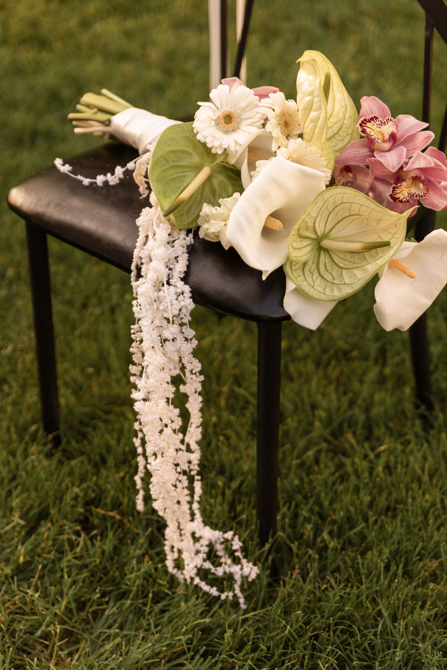 Close-up of floral wedding decorations with white and pink flowers draped elegantly over a metal railing on grass.