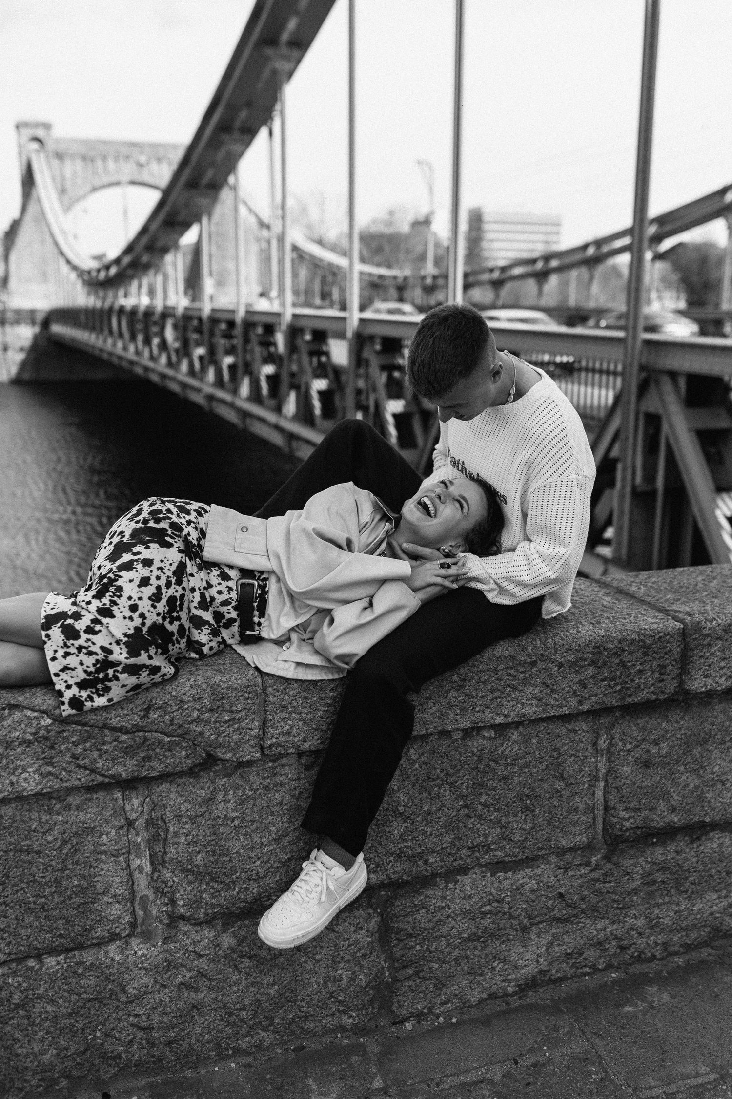 Black and white romantic couple portrait on bridge wall with cityscape in background.