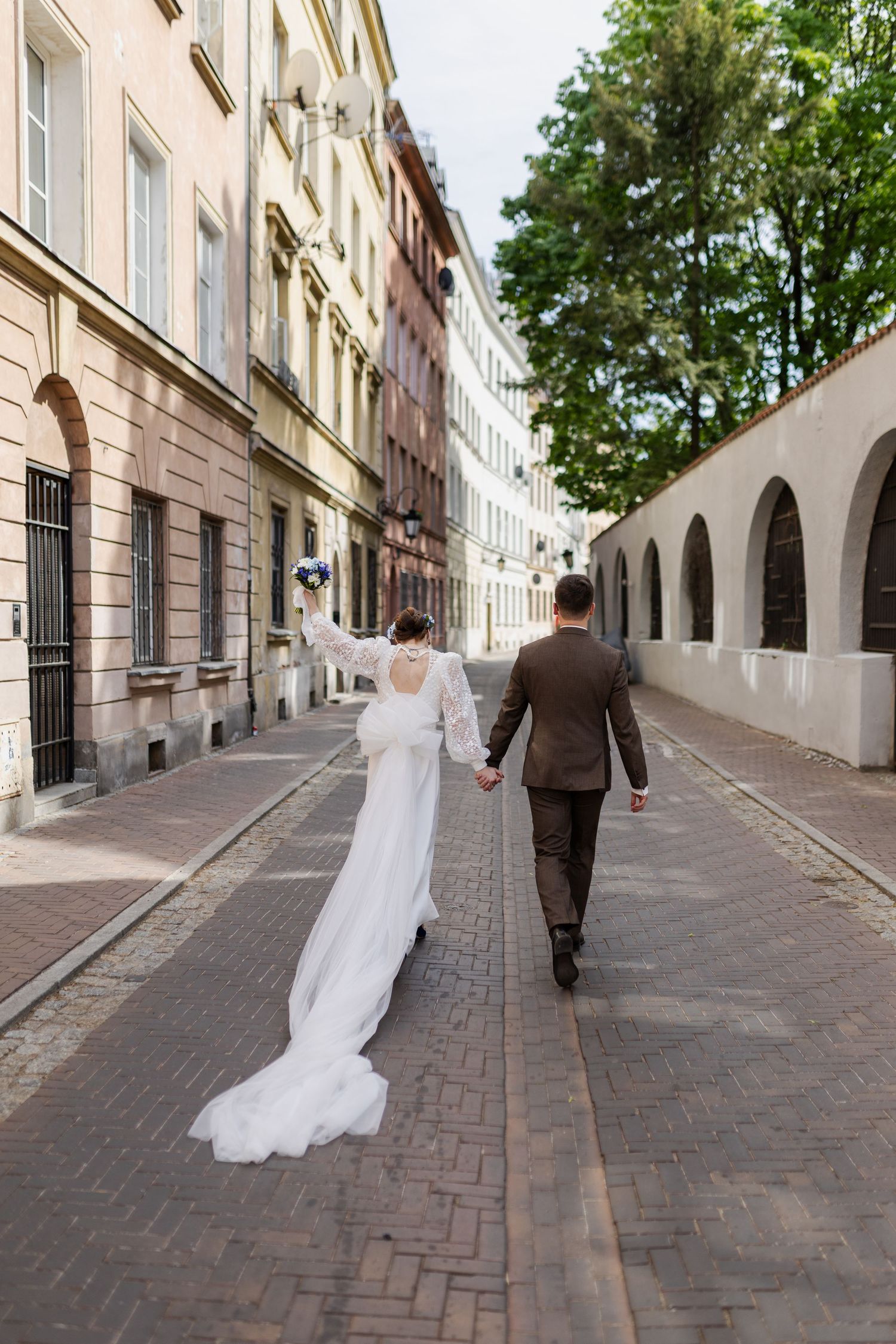 A couple holding hands and walking down a charming cobblestone street lined with historic buildings and arched walls.