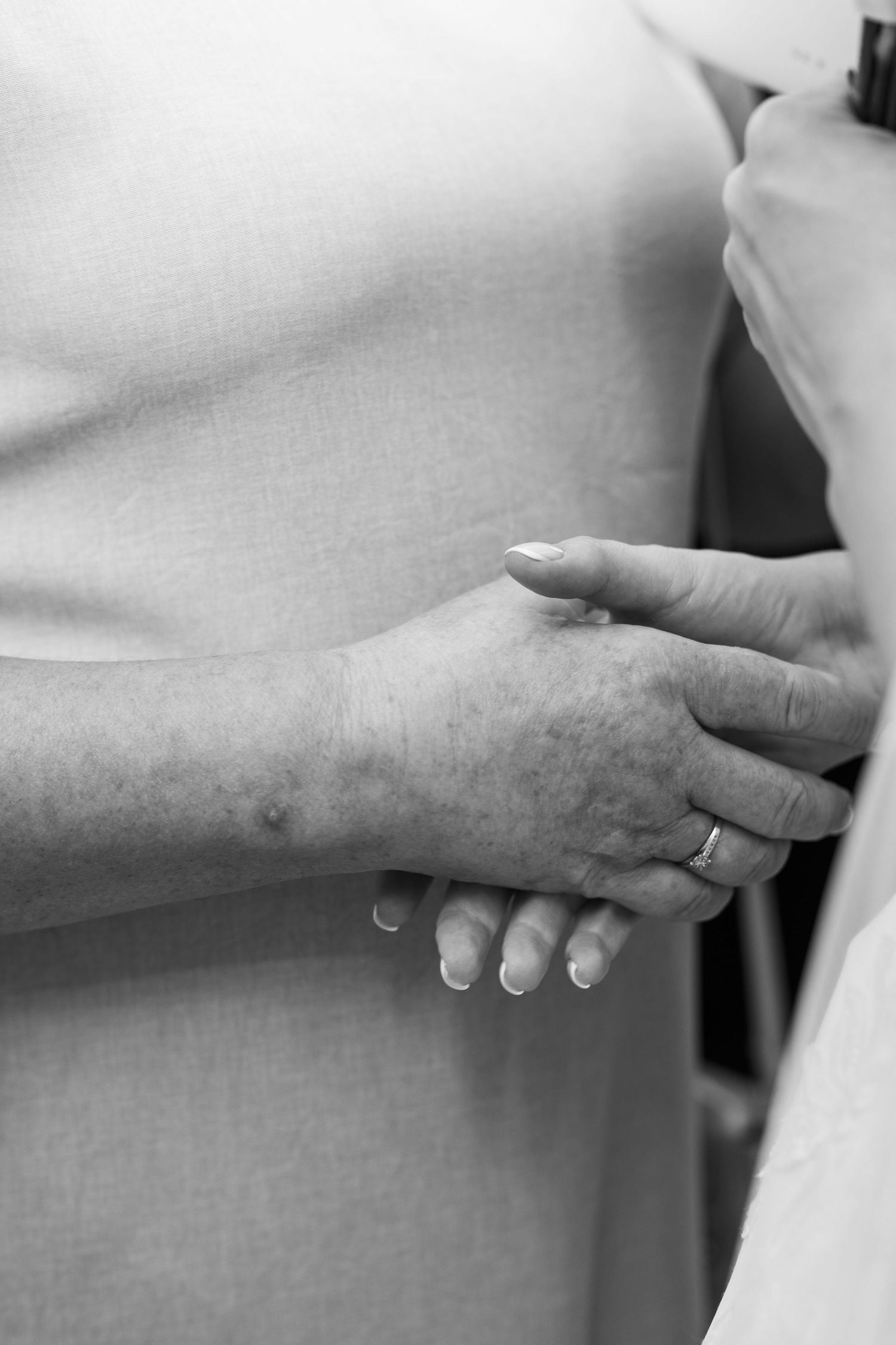 A close-up black and white photograph shows two hands gently clasped together in a tender moment.