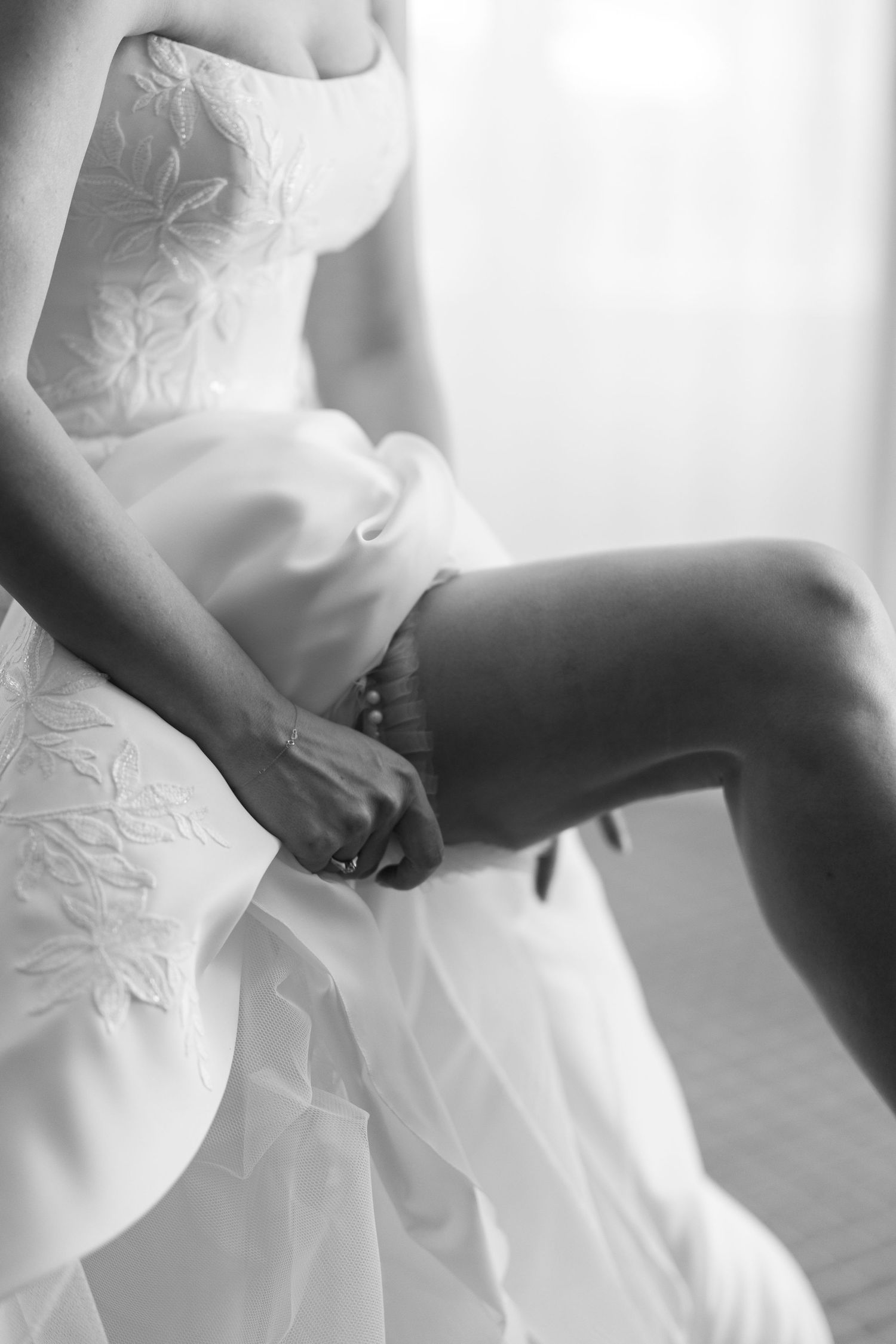 A series of black and white photos showing the delicate details of a white wedding dress fabric and silhouette.