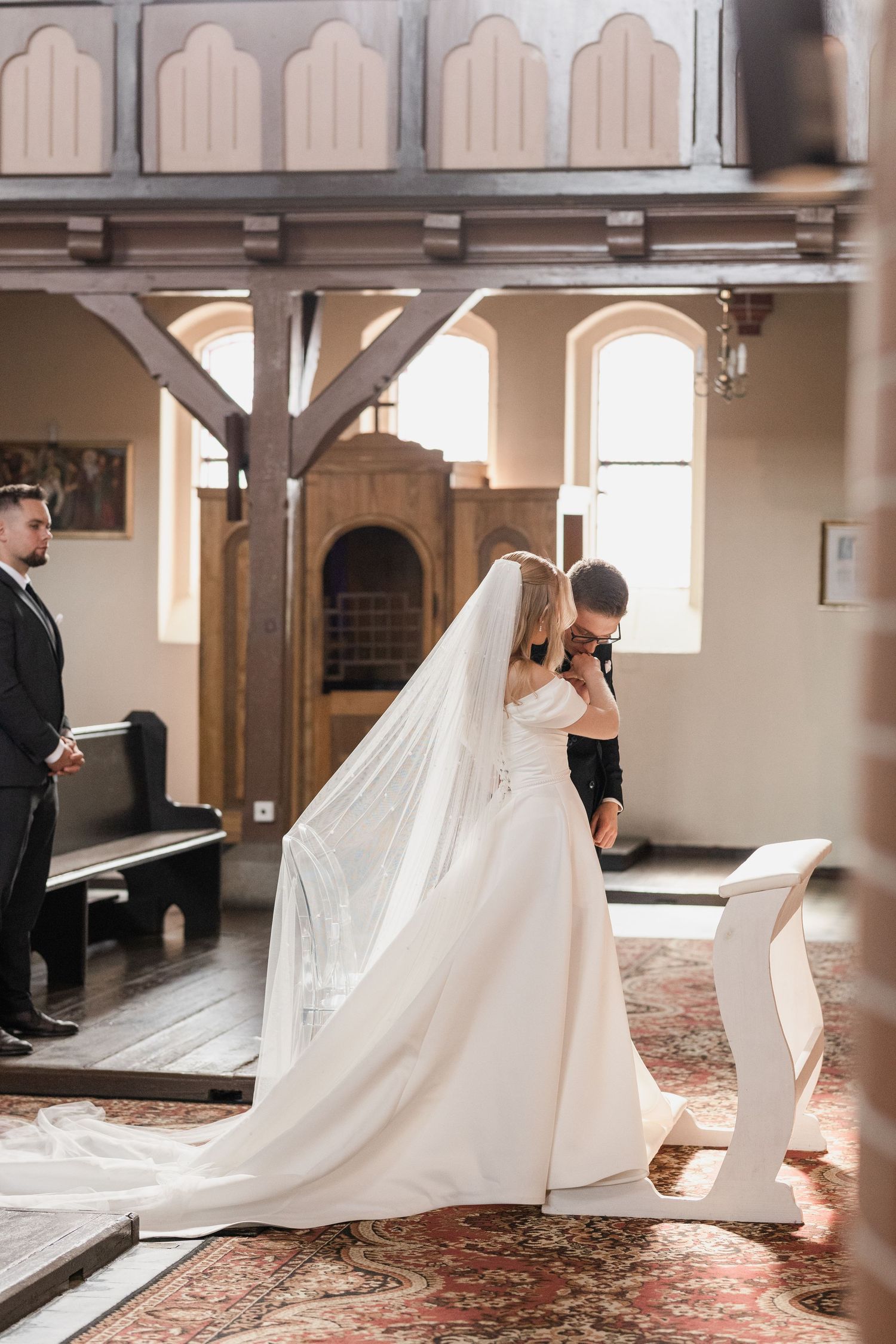 A flowing cathedral veil trails behind a bride in an elegant white wedding dress as she walks across a church floor.