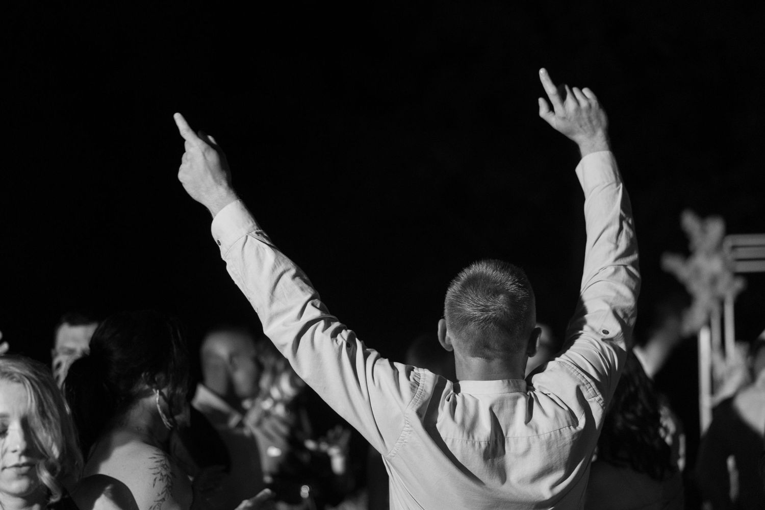 Man raising both arms at a lively event, captured in black and white photography.
