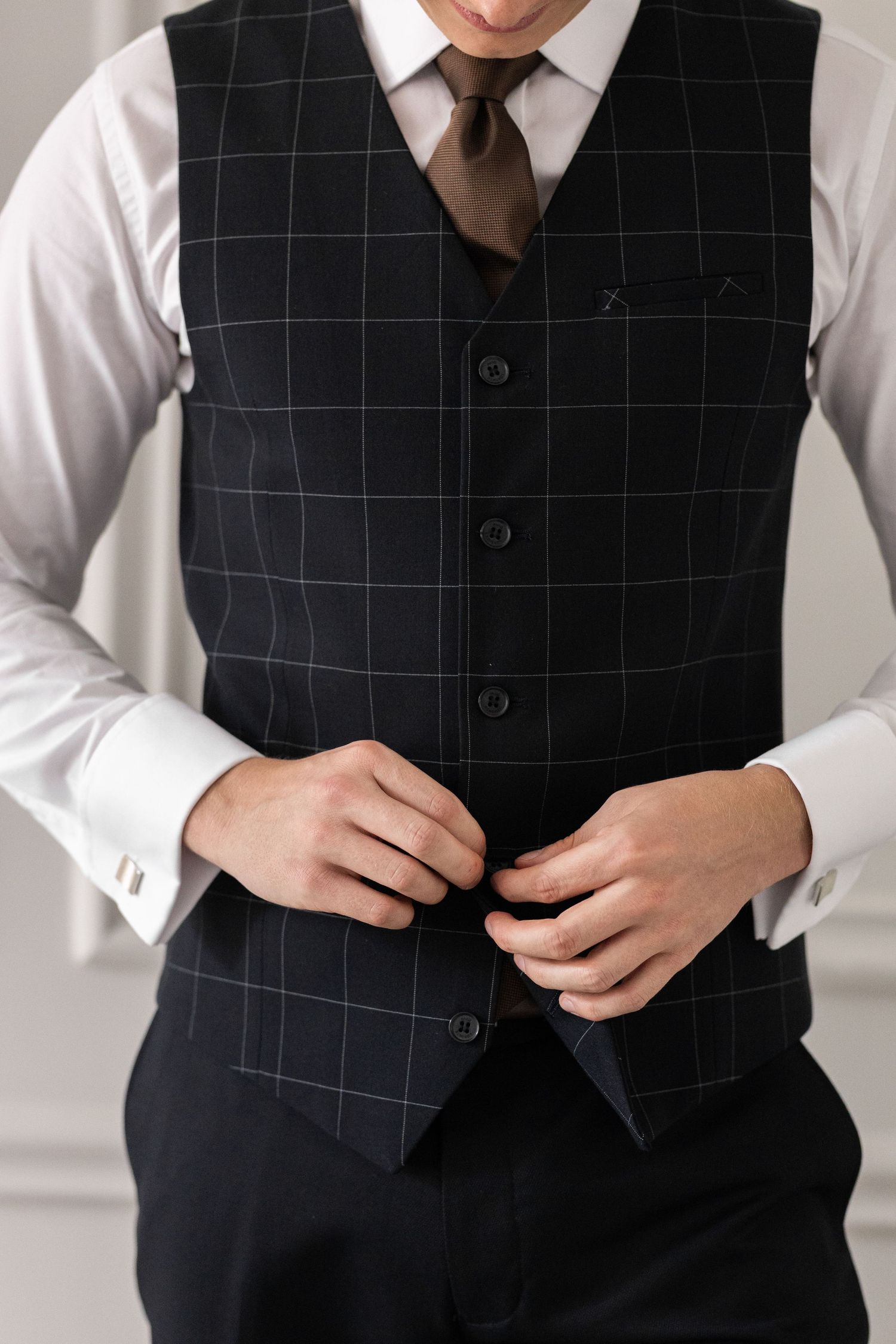 Close-up view of a black windowpane check suit vest being buttoned over a crisp white dress shirt.