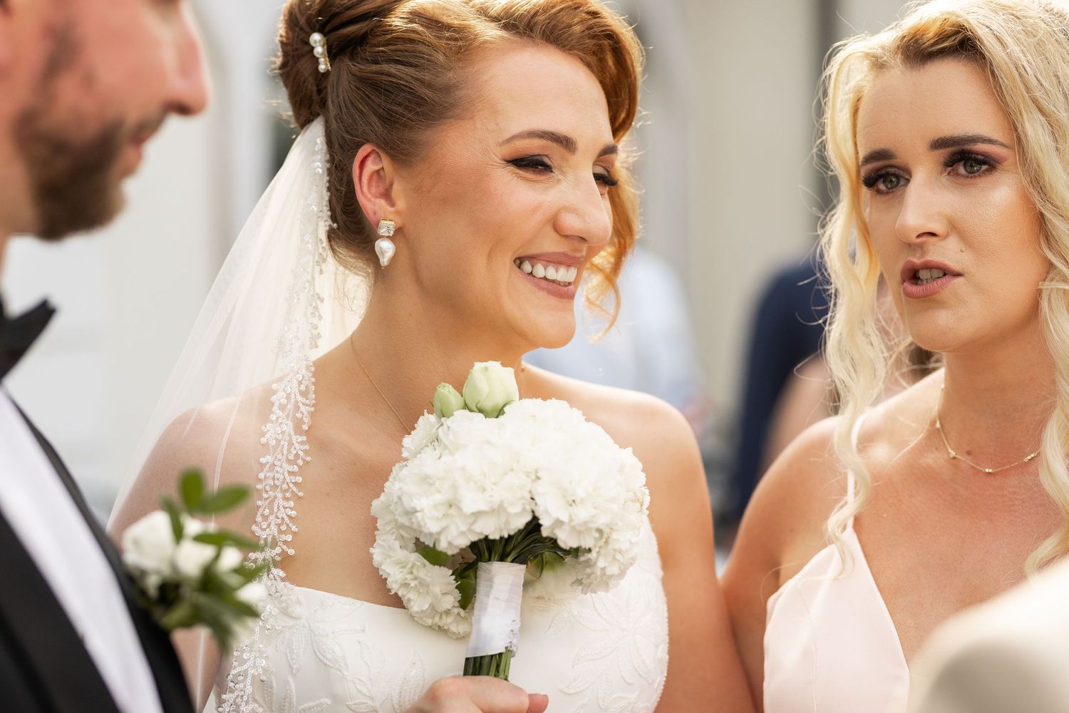 A group of bridesmaids in white dresses share joyful moments at a wedding celebration.