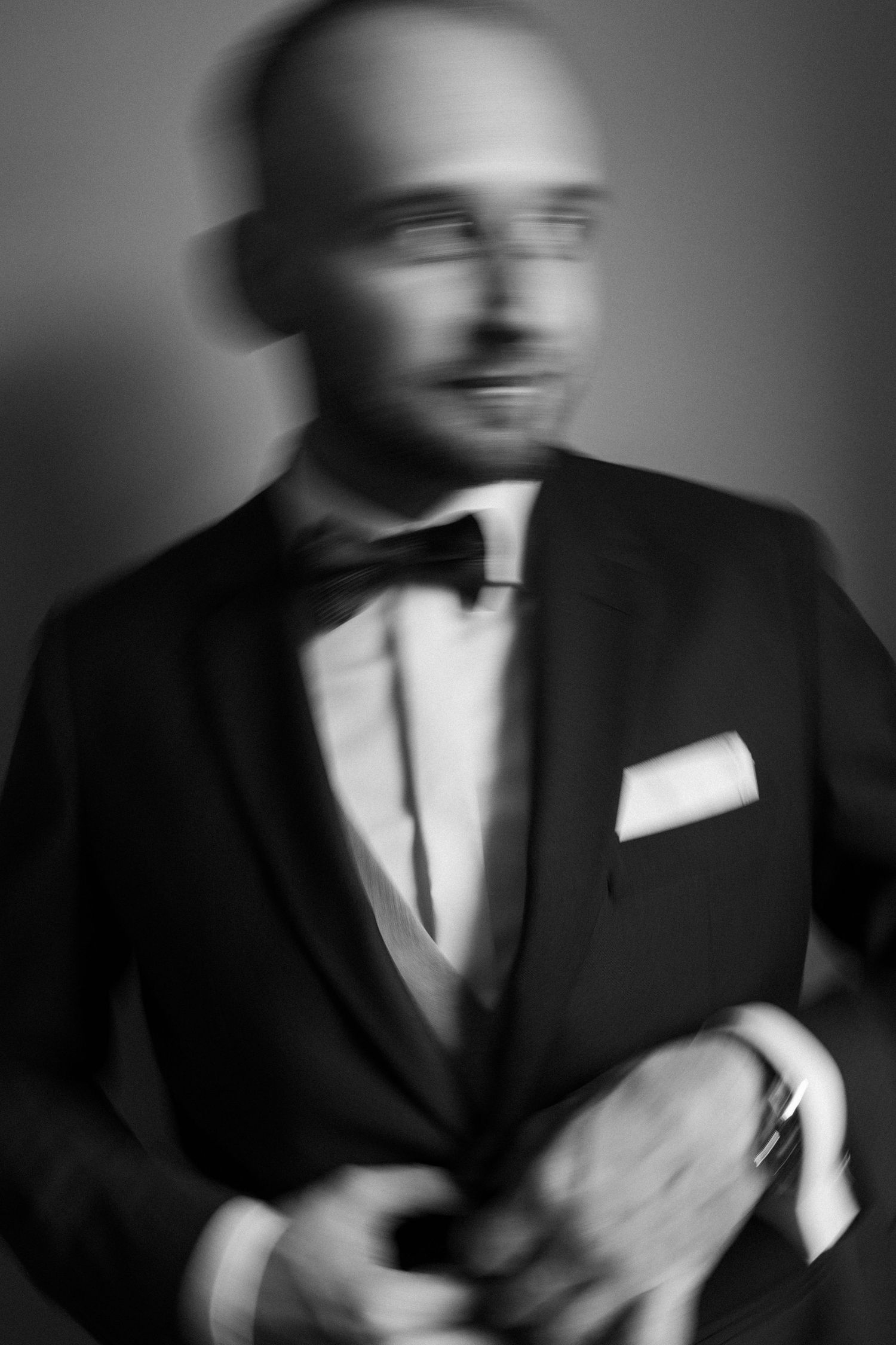 Artistic black and white portrait of a person in formal wear with bow tie and pocket square, creating a motion blur effect.