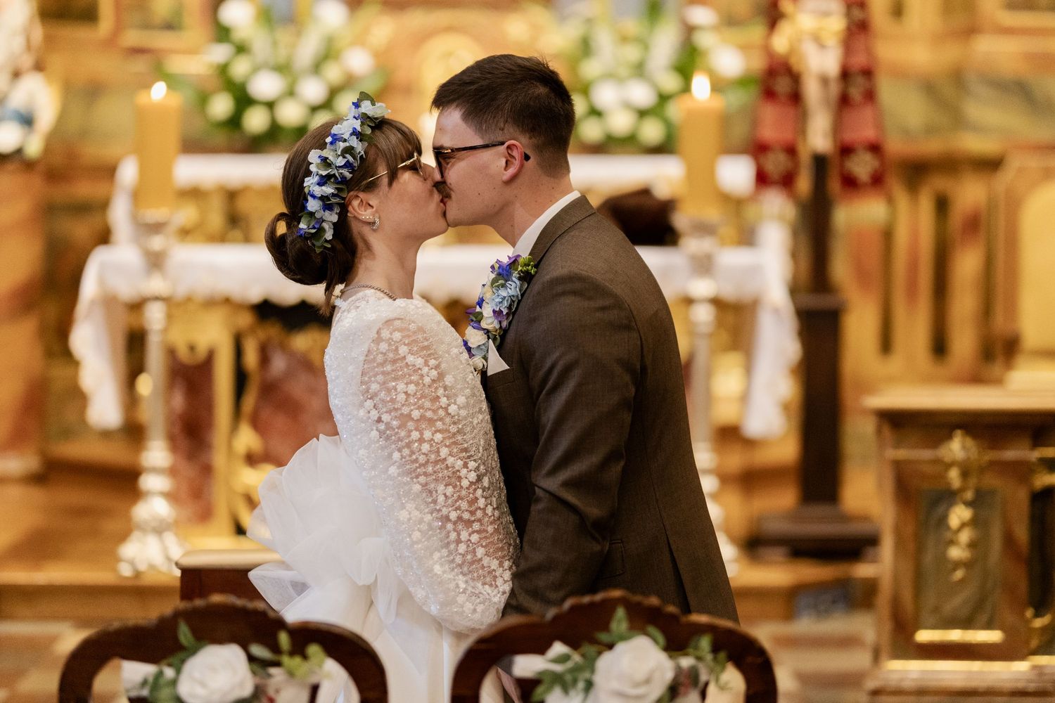 Romantic wedding moment inside ornate church with golden altar and decorative floral arrangements.