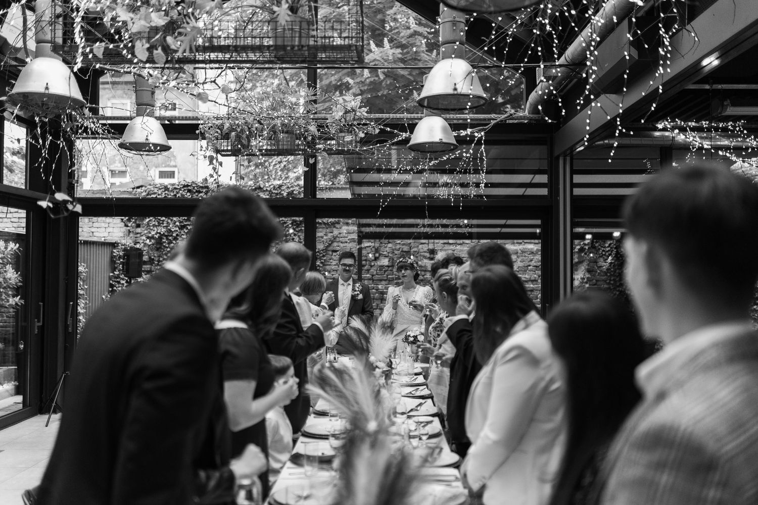 A black and white photo of people mingling at a festive indoor gathering with hanging lights and decor visible above.
