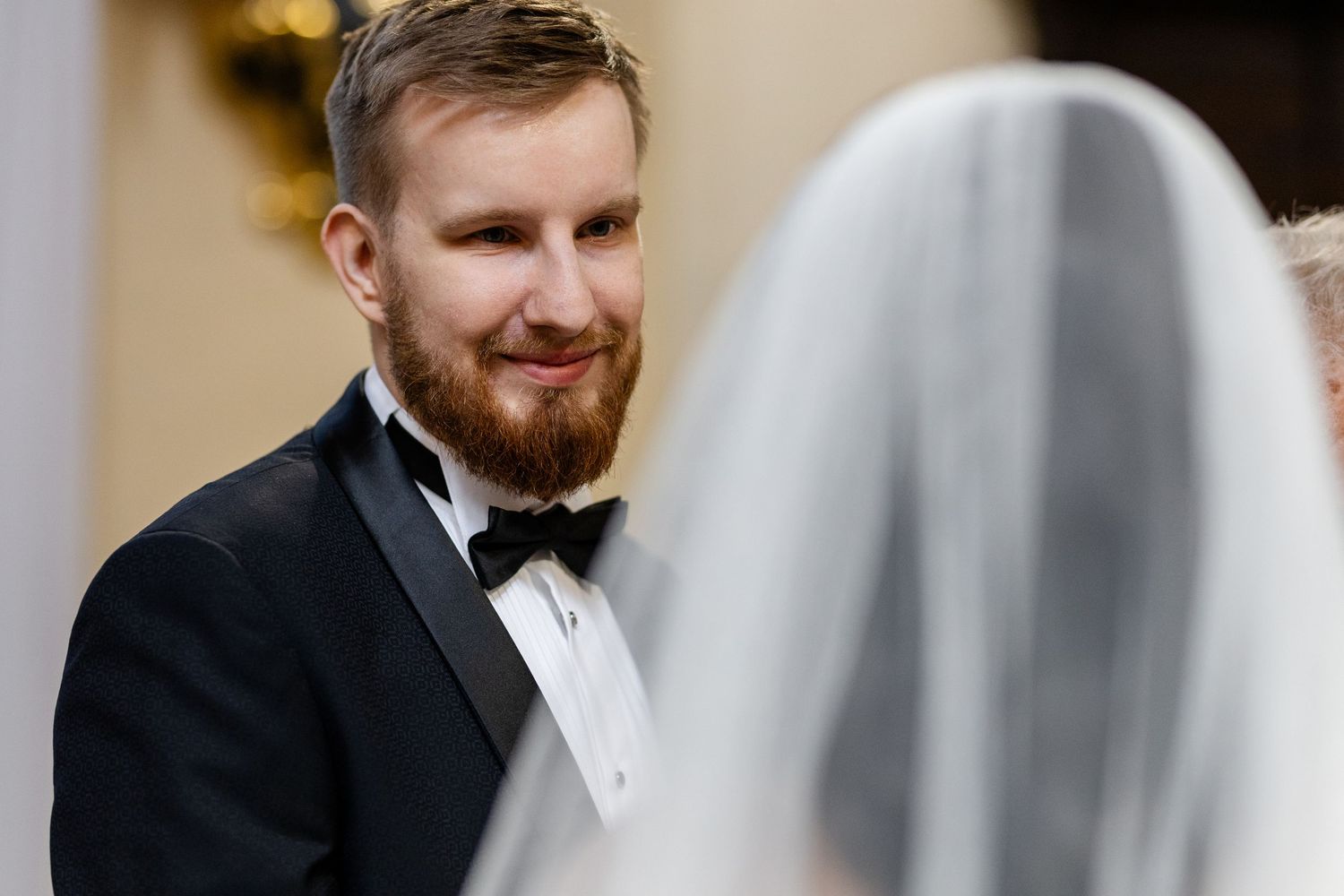 An elegant wedding moment as a groom in a black tuxedo shares a heartfelt first look with his veiled bride.